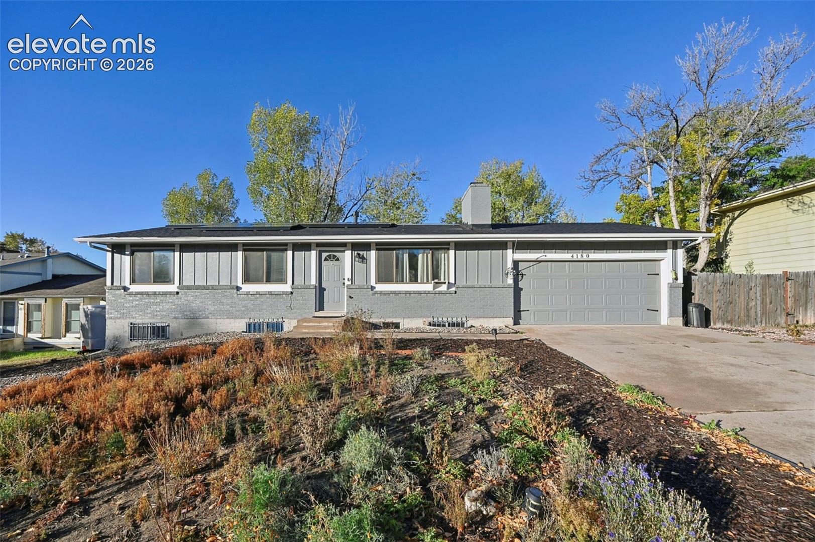 Single-story residence featuring a gray brick and vertical siding exterior, a two-car attached garage, a concrete driveway, and a central chimney