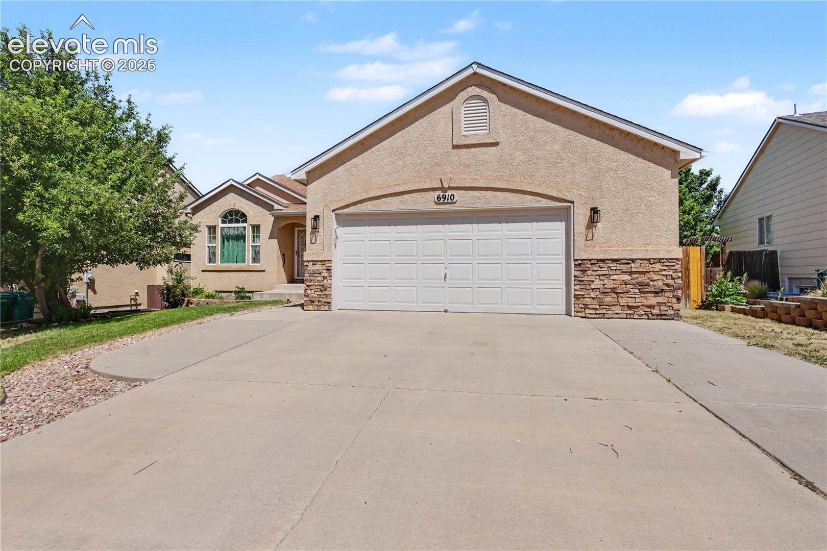 Stucco exterior with a stone veneer accent, attached garage, and a concrete driveway
