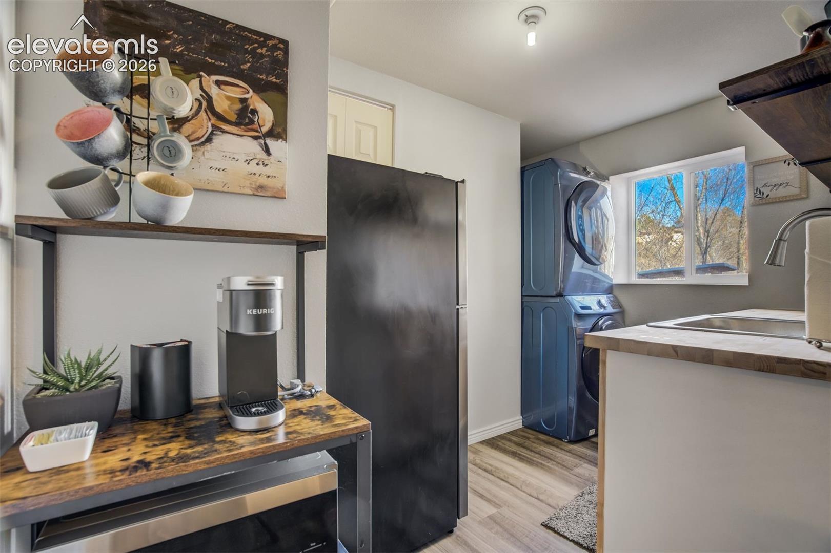 Stacked washer and dryer, stainless steel sink, wood-finish countertops, wood-finish flooring, and white cabinetry