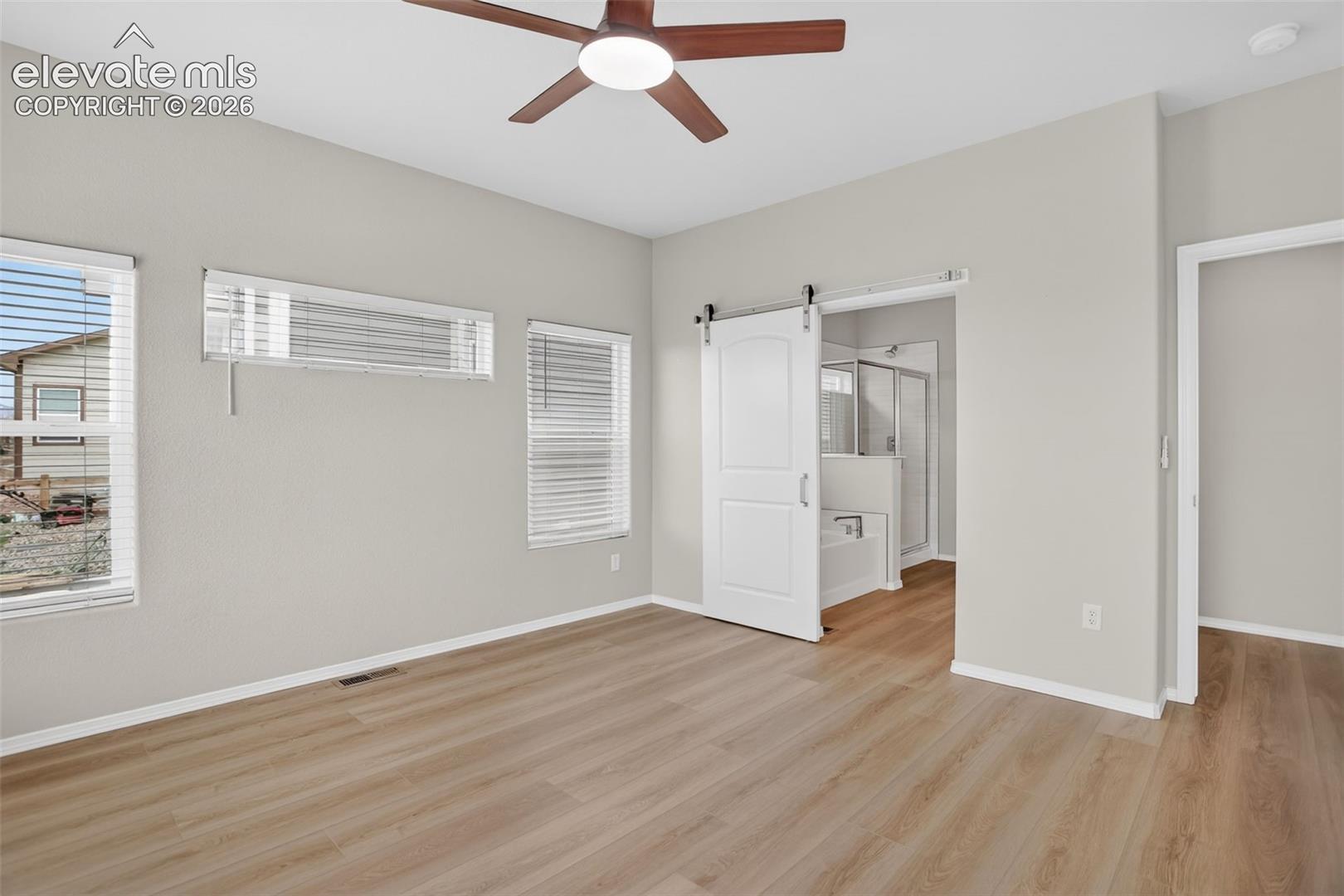 Neutral-toned room featuring wood-finish flooring and a ceiling fan with integrated lighting