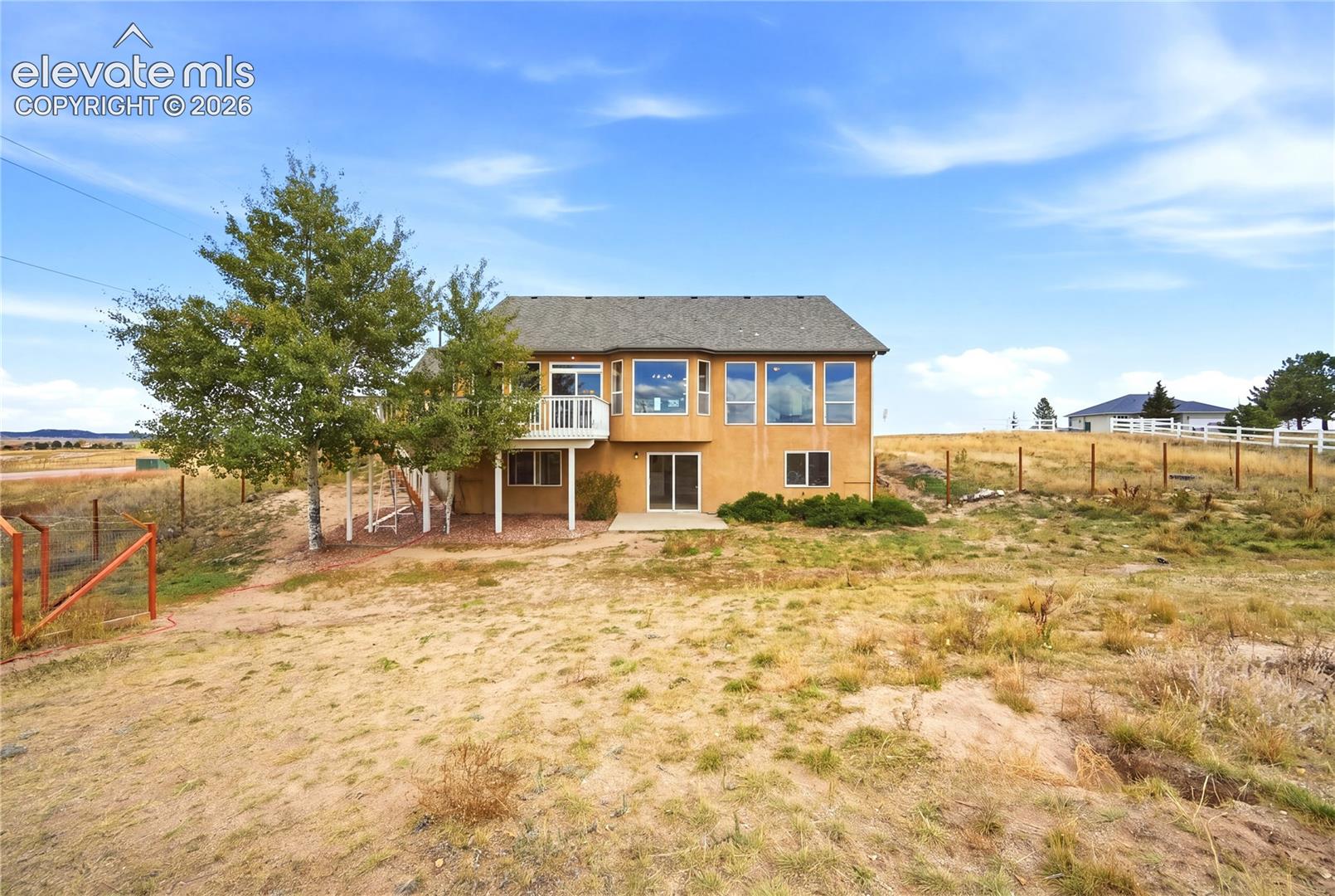 Stucco exterior residence featuring a raised wood deck, expansive multi-pane windows, and sliding glass door entry set on a large acreage lot