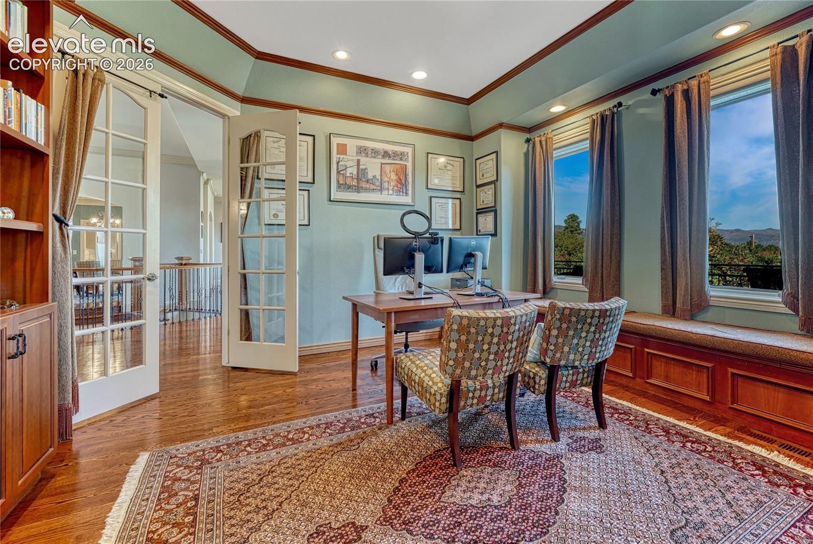 Wood-finish flooring, built-in cabinetry, tray ceiling with recessed lighting, double French doors, and a wood-paneled window seat