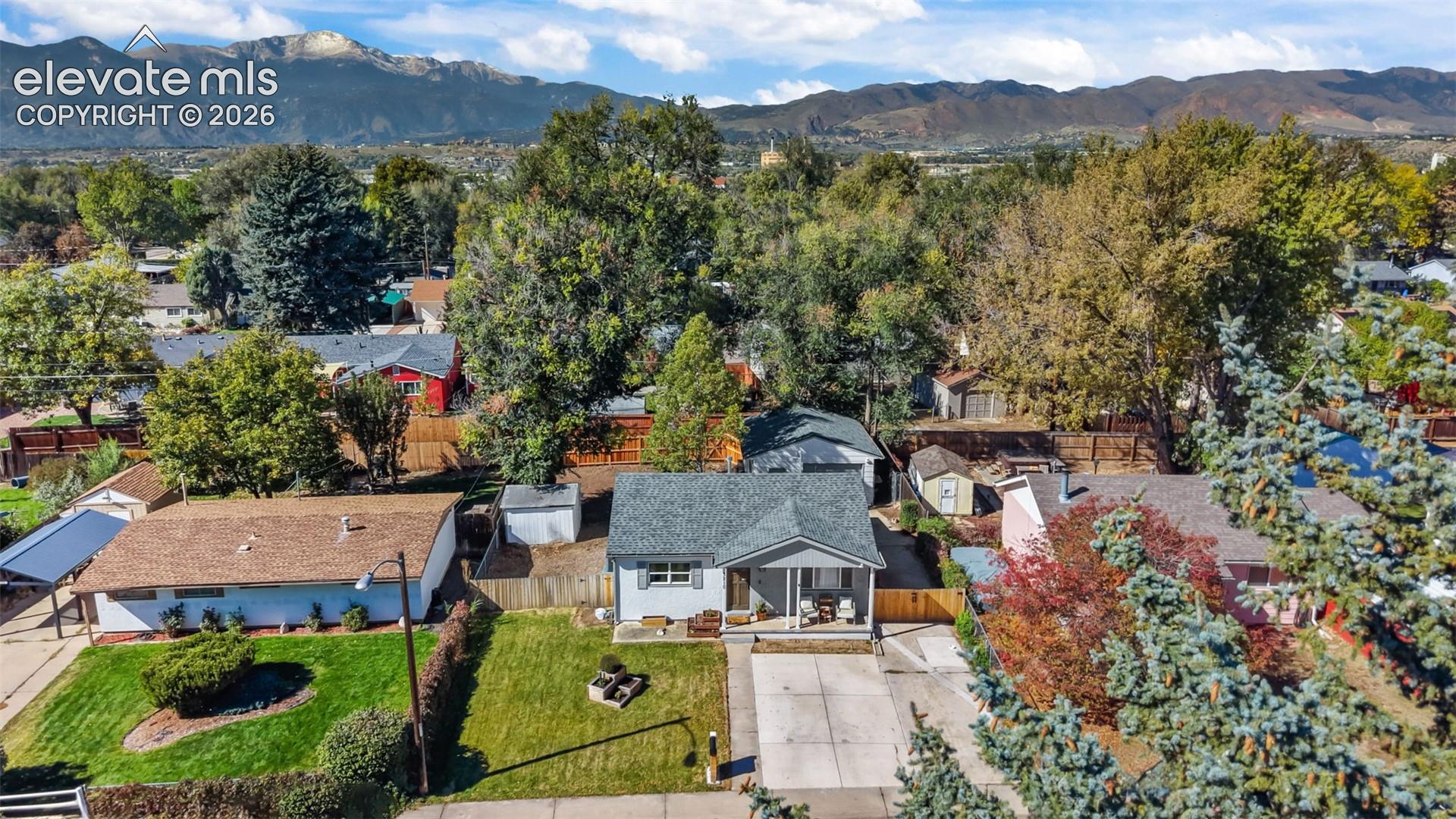 Single-story residence featuring a gray exterior, gabled roofline, concrete driveway, and a front lawn, set against a backdrop of mountain scenery