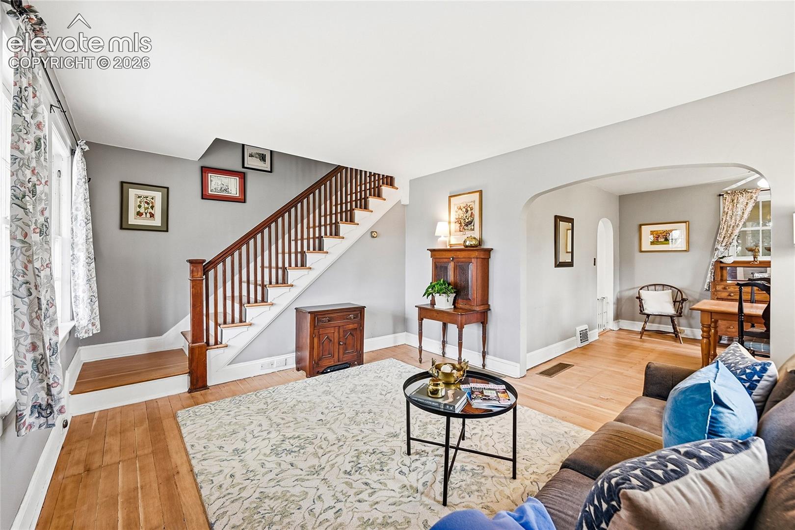 Hardwood flooring, wood-capped staircase with railings, arched wall opening, and multi-pane windows
