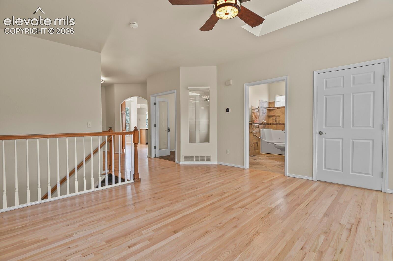 Hardwood flooring, railed staircase with decorative wood balusters, vaulted ceiling with integrated light-fixture fan, and interior arched architectural detailing