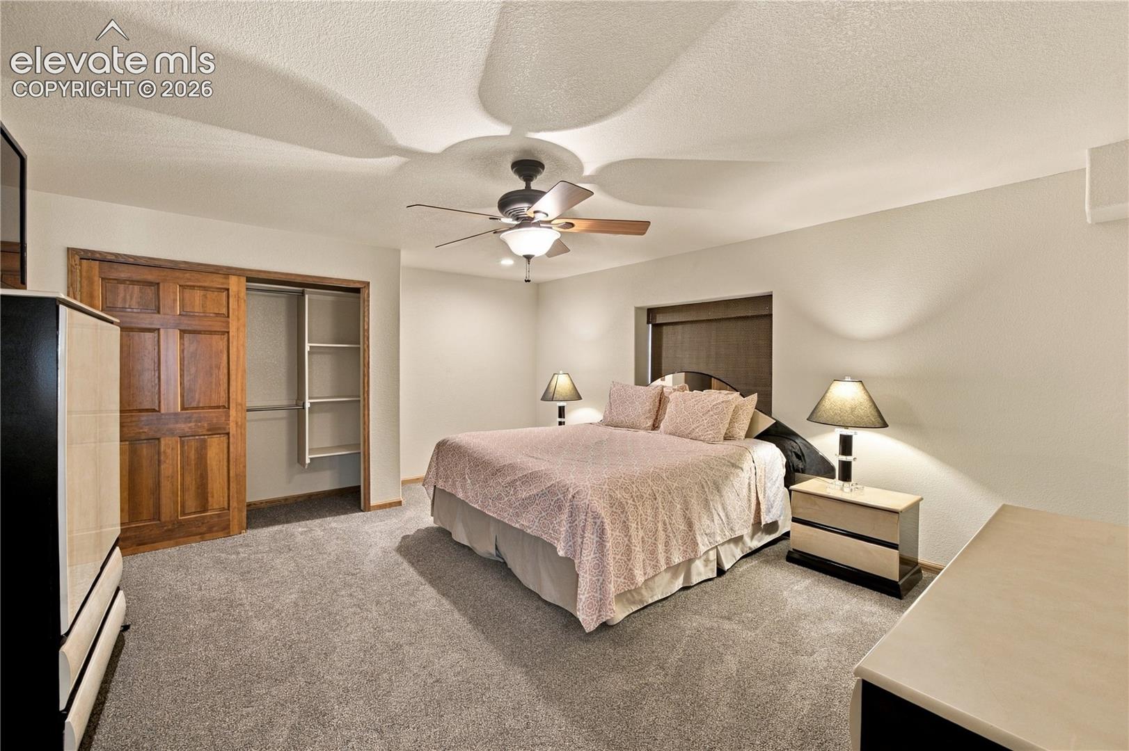 Neutral wall-to-wall carpeting, ceiling fan with integrated lighting, and natural wood-finish sliding closet doors featuring interior built-in shelving