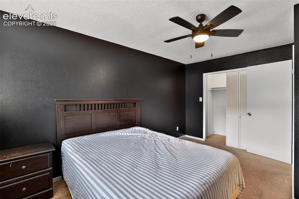 Bedroom featuring dark textured walls, carpet flooring, and a ceiling fan with integrated lighting
