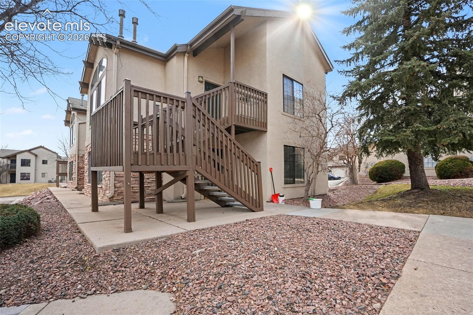 Multi-level exterior featuring stucco siding, stone veneer accents, wood-railing staircases, and second-story balcony