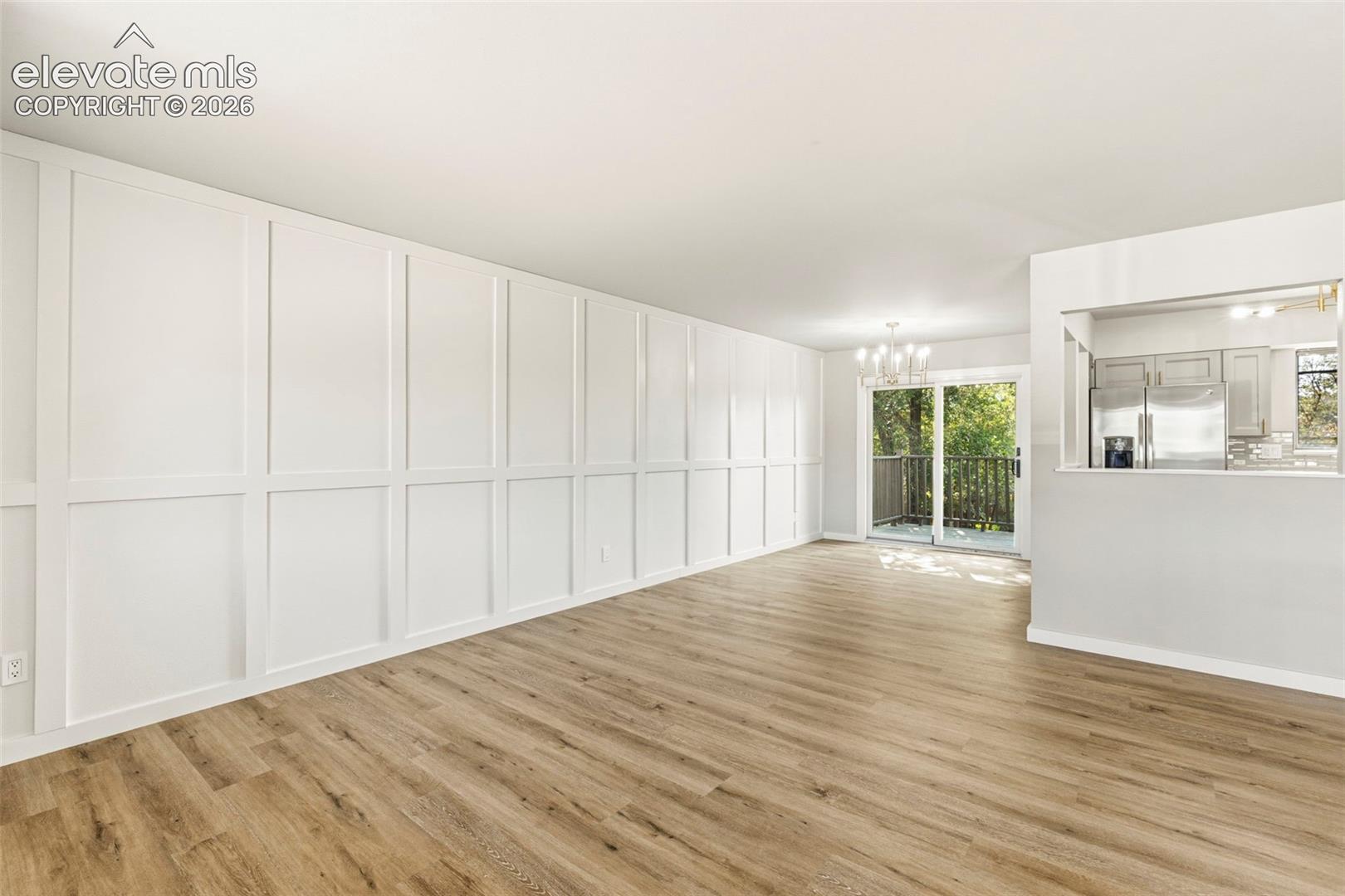 Living area featuring a full wall of decorative paneling, luxury vinyl plank flooring, and a sliding glass door opening to an outdoor deck