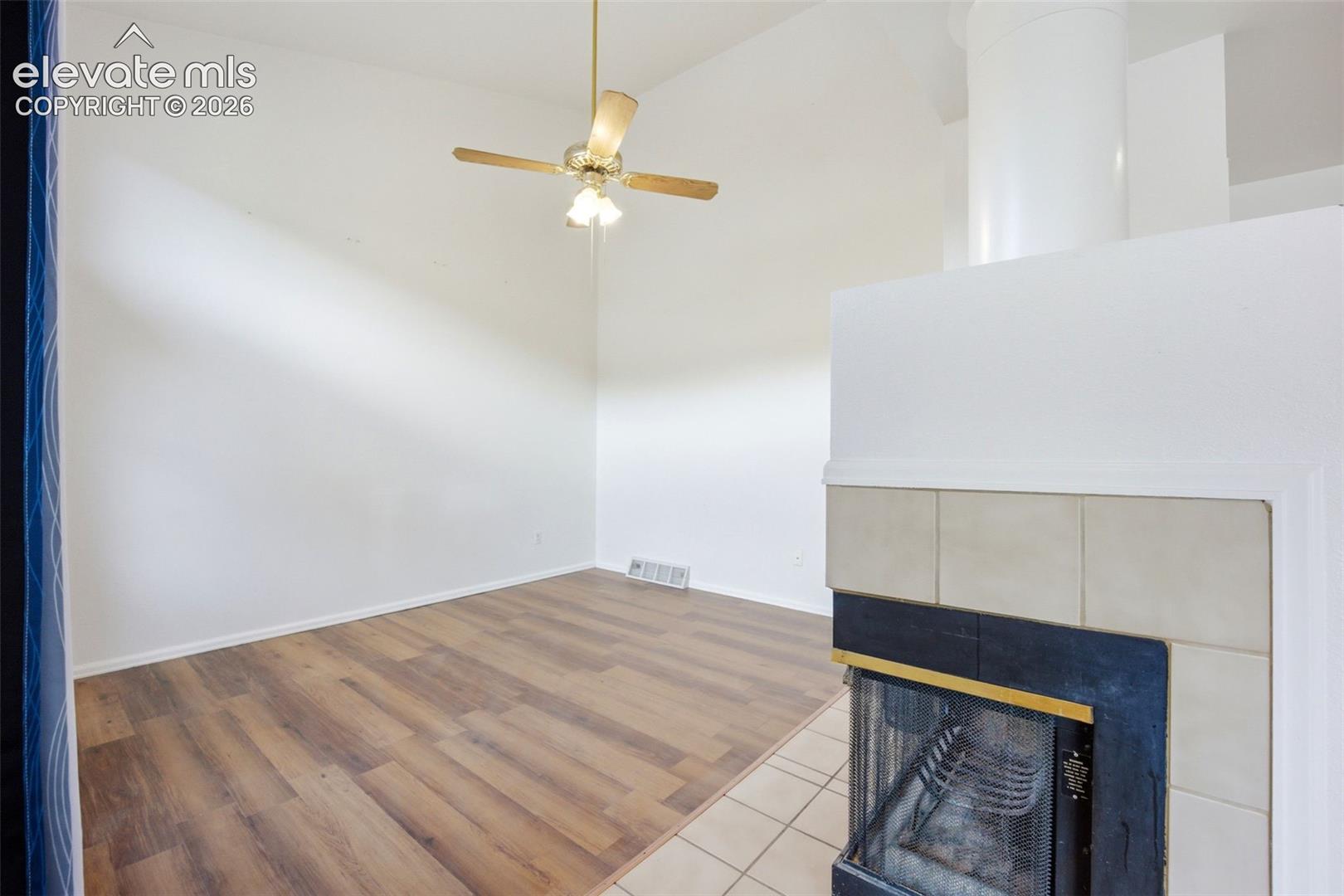 Vaulted ceilings, wood-finish flooring, and a fireplace with a light-tone tile surround and black metal trim