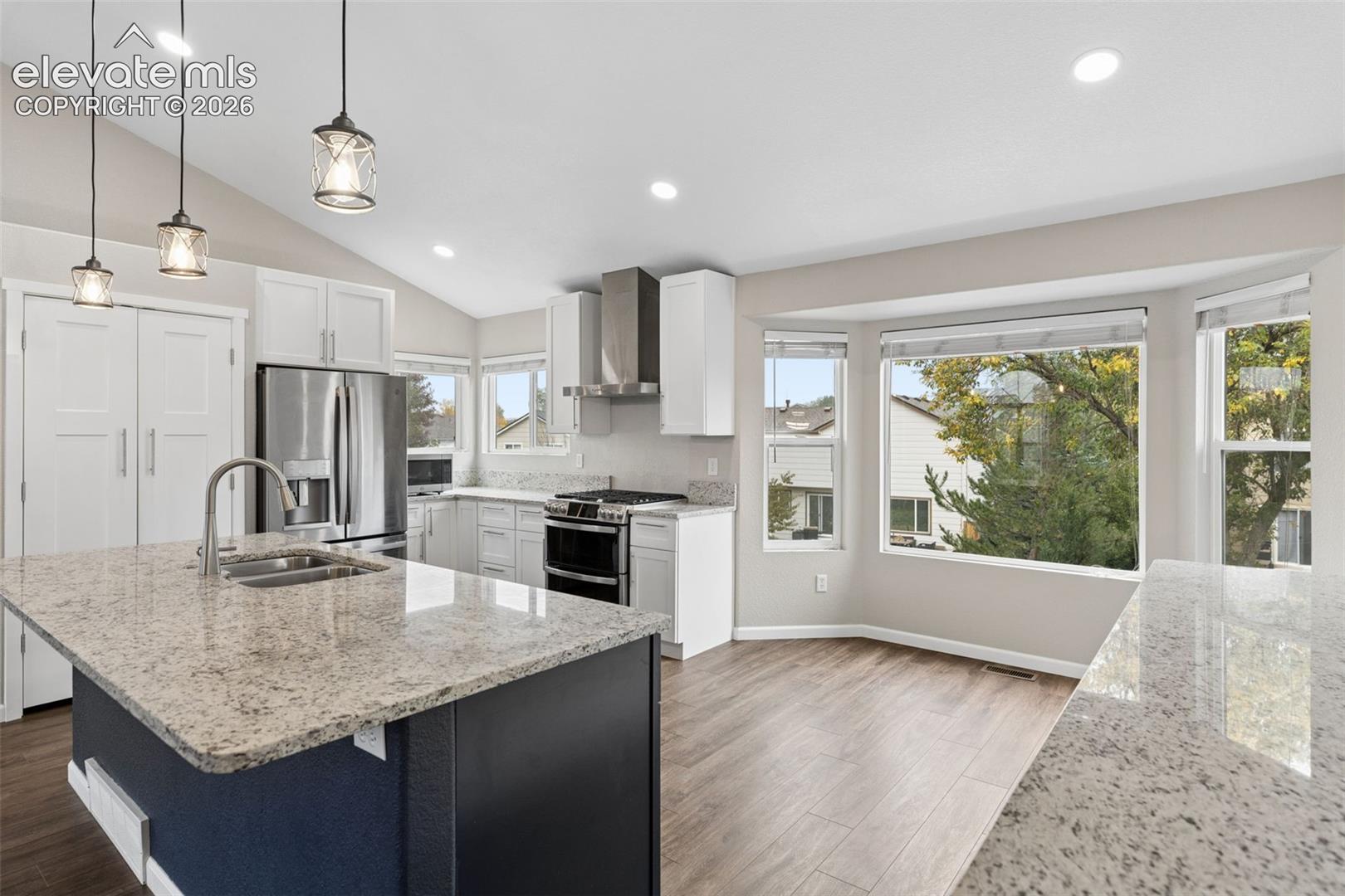 Kitchen featuring a central island with stone countertop, stainless steel appliances, white cabinetry, vaulted ceilings, and wood-finish flooring