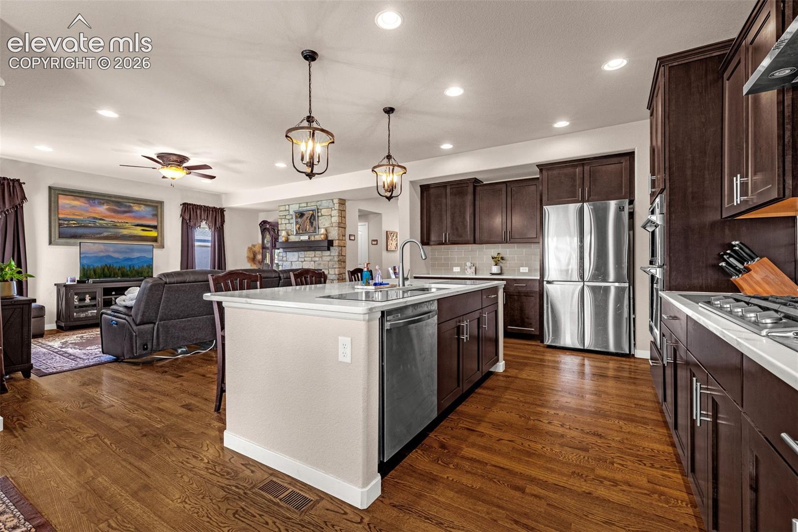 Kitchen featuring dark wood cabinetry, a central island with an integrated sink, stone-finish countertops, stainless steel appliances, and wood-finish flooring