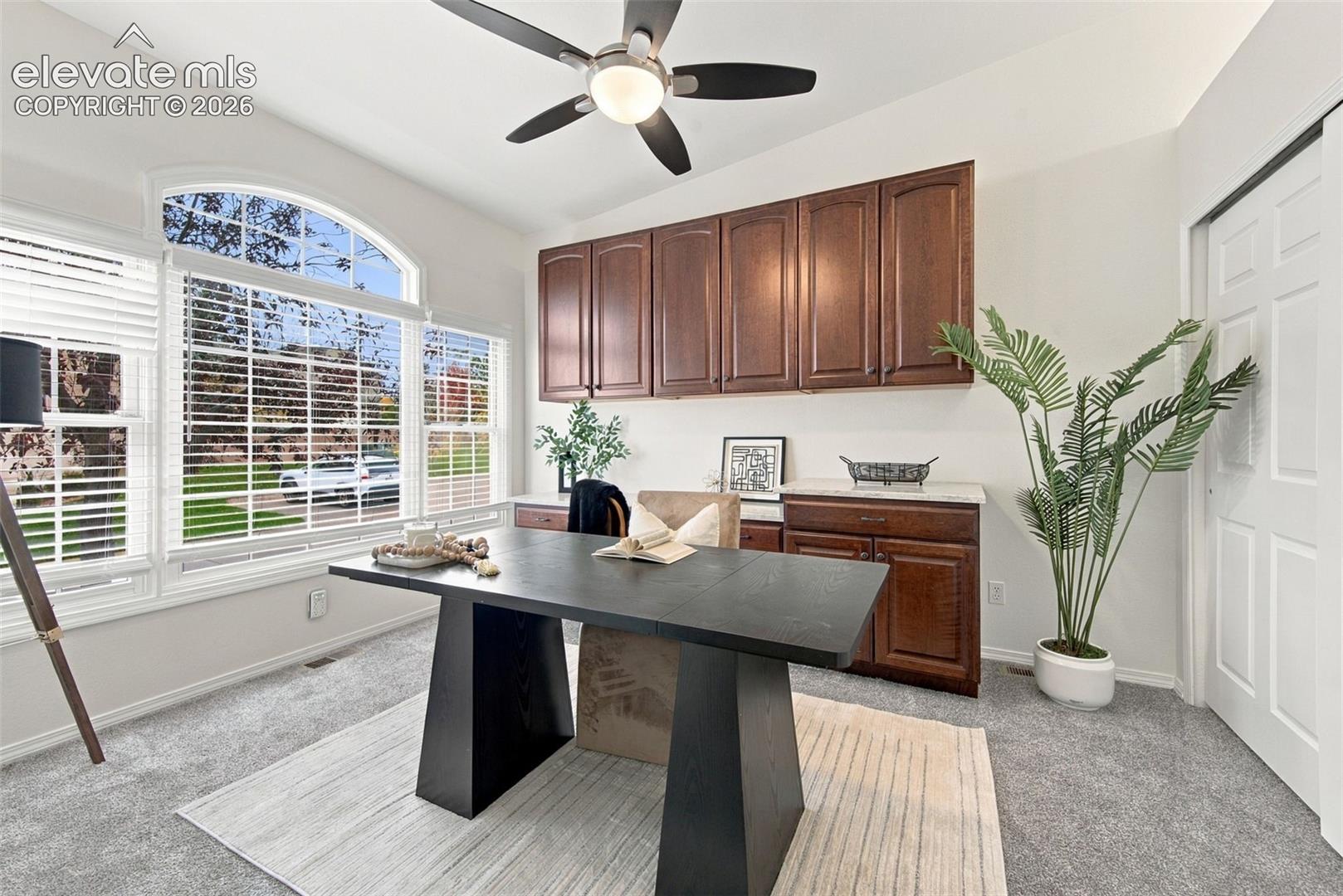 Built-in stained wood cabinetry, vaulted ceiling with integrated light fixture and ceiling fan, large arched window, and carpeted flooring