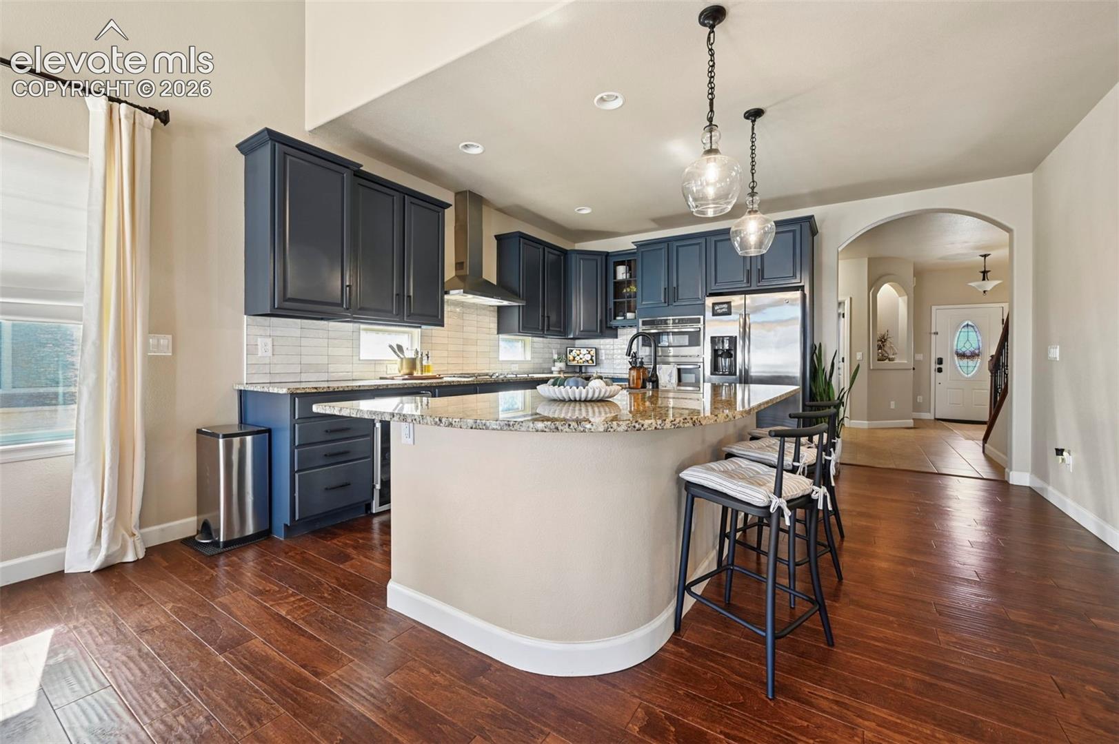Kitchen featuring dark cabinetry, stone-finish countertops, a central island with bar seating, wood-finish flooring, and pendant lighting