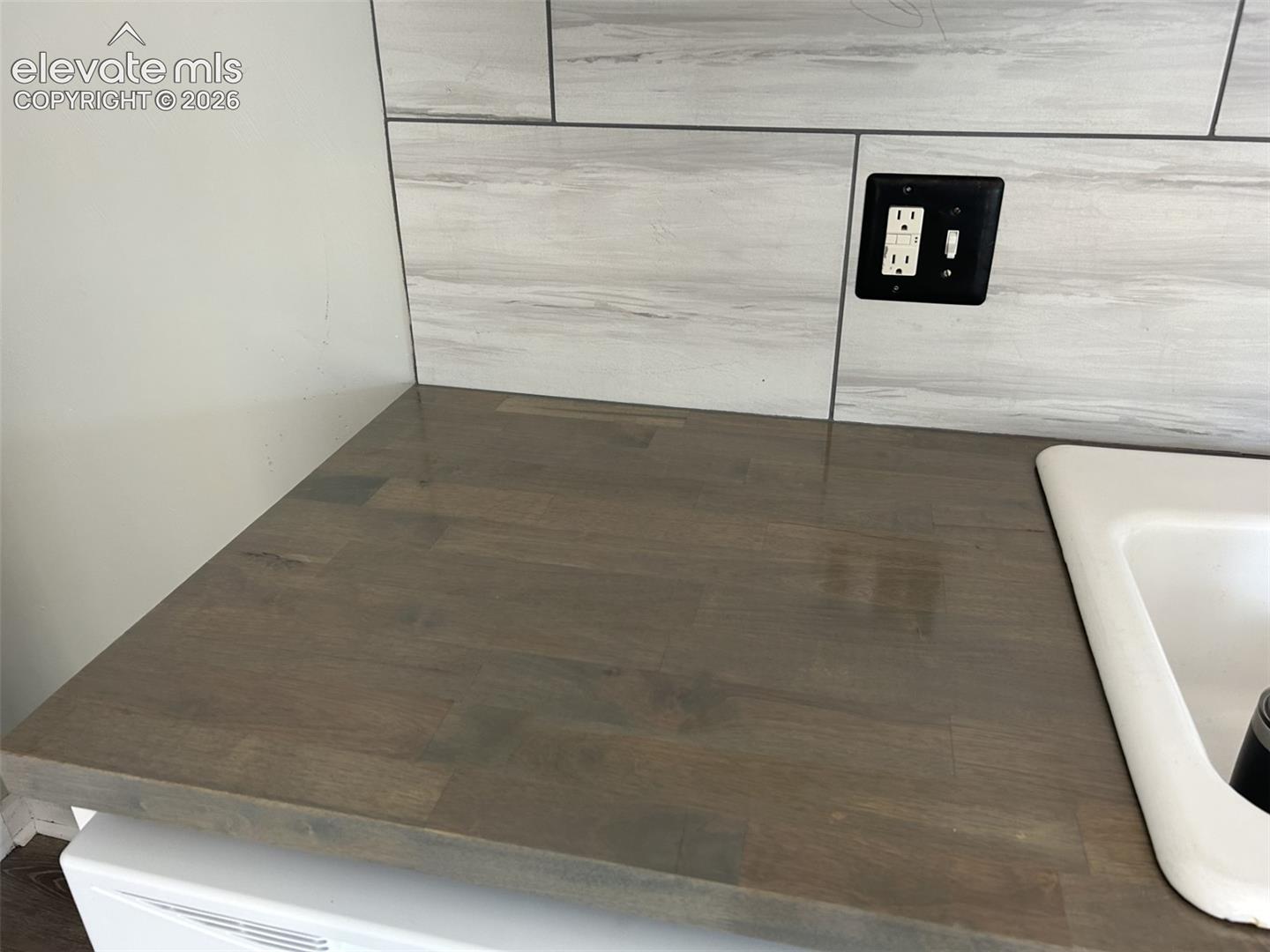 Wood-finish countertop with an integrated white sink and a tiled backsplash