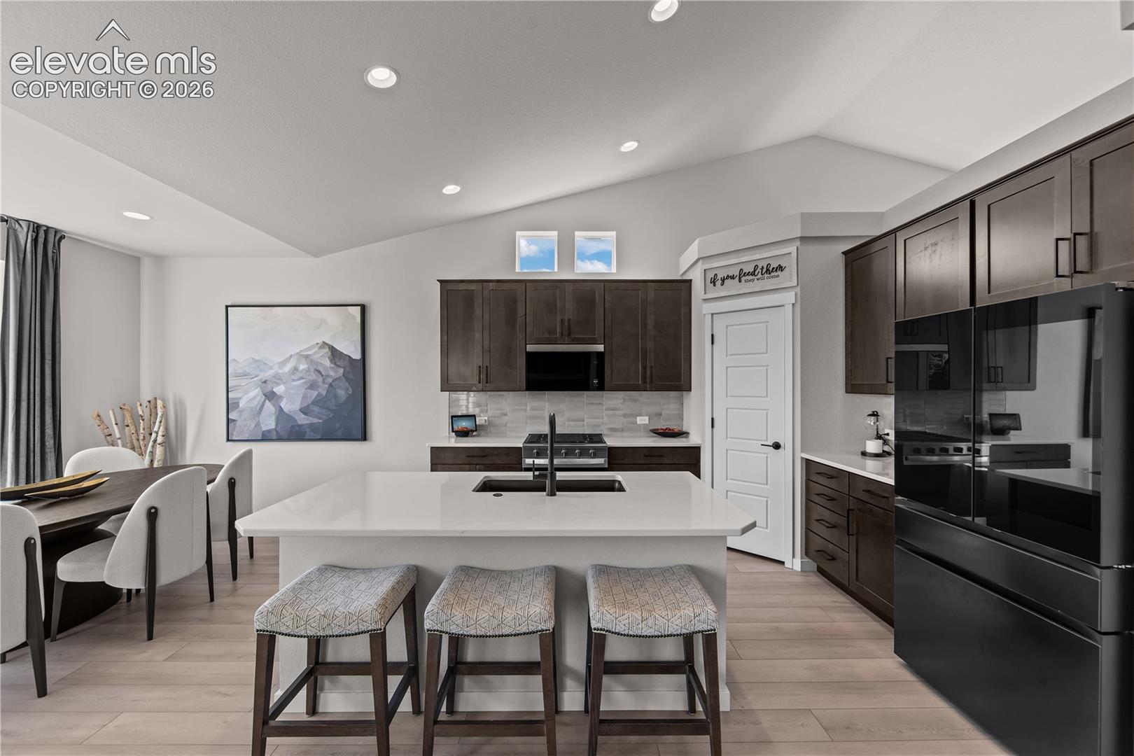 Kitchen featuring dark-toned cabinetry, quartz countertops, a center island with a drop-in sink, recessed ceiling lighting, and wood-finish flooring
