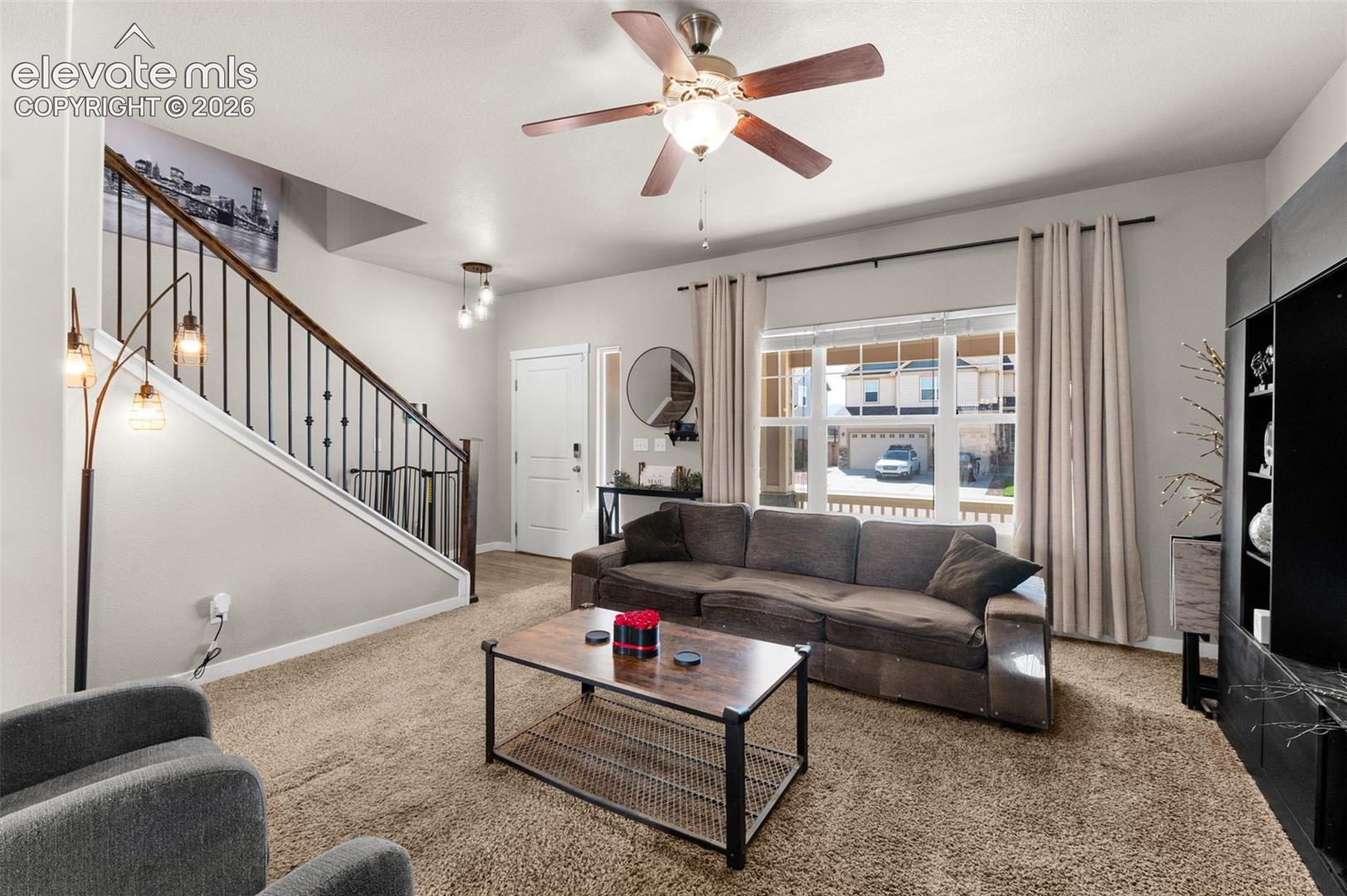 Living area featuring a multi-pane window, staircase with iron balusters, ceiling fan, and pendant lighting