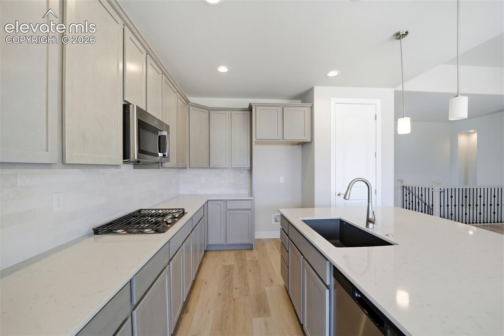 Kitchen featuring shaker-style cabinetry, quartz countertops, a gas cooktop, undermount rectangular sink with high-arc faucet, and wood-finish flooring
