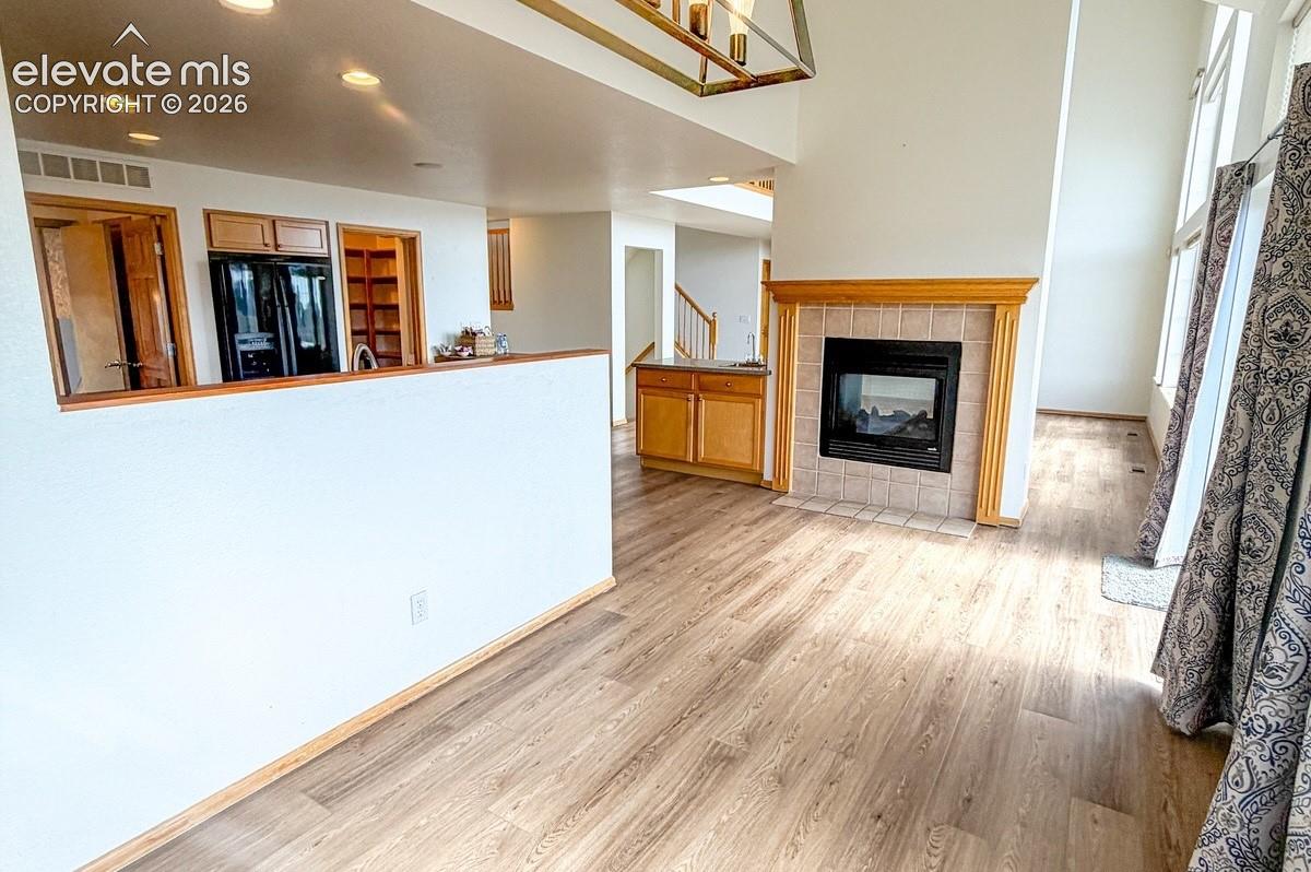 Wood-finish flooring, recessed lighting, gas fireplace with tile surround and wood mantel, light wood cabinetry, and large windows