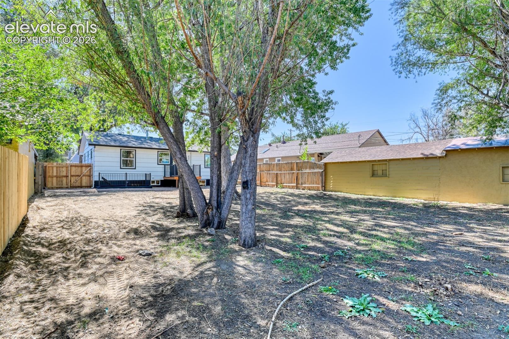 Expansive backyard featuring mature trees, a wood privacy fence, and a rear deck with dark railing