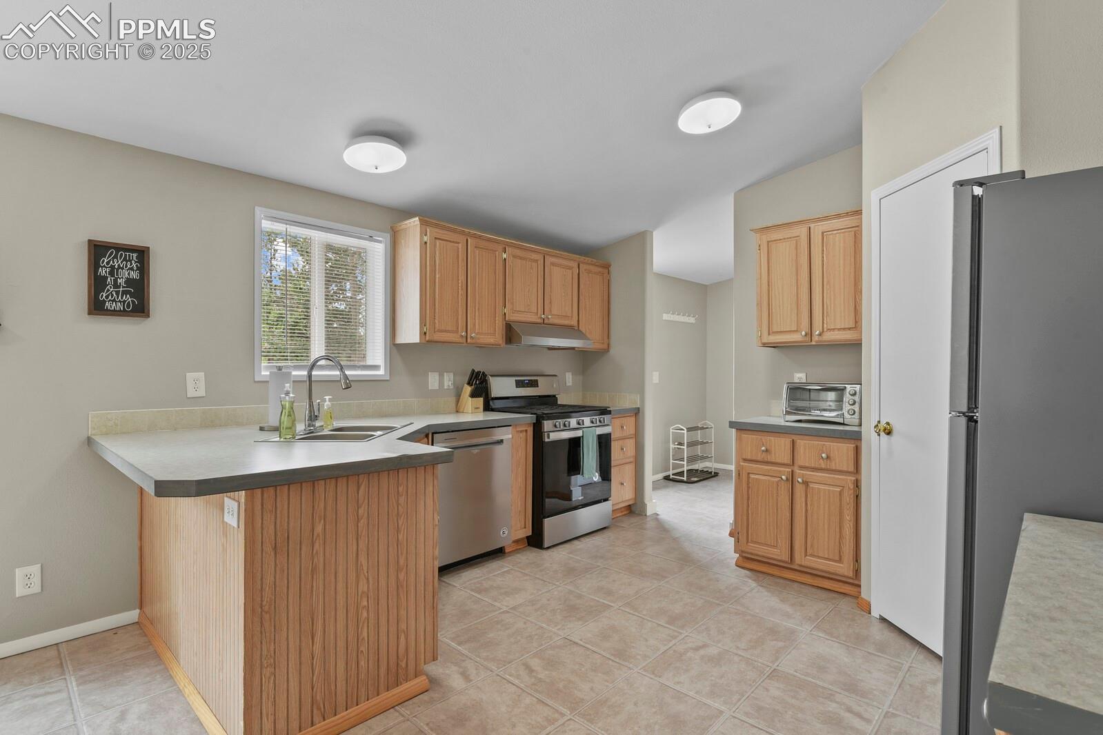 Kitchen featuring appliances with stainless steel finishes, a peninsula, light tile patterned flooring, under cabinet range hood, and light countertops