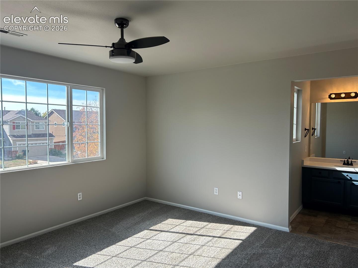 Neutral interior space featuring wall-to-wall carpeting, a multi-pane window, and a matte black ceiling fan with integrated lighting