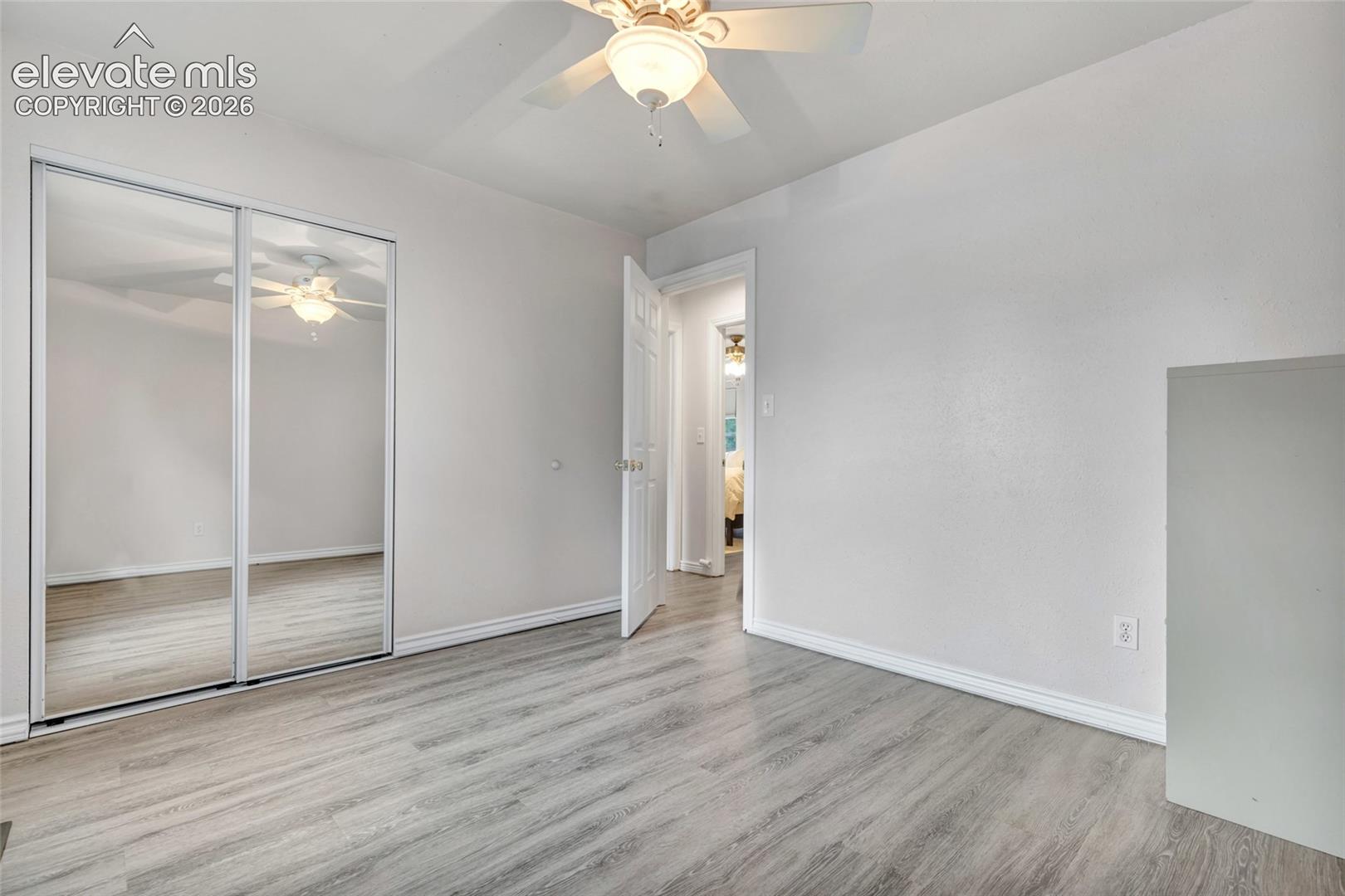 Room with wood-finish flooring, white walls, and a ceiling fan with light fixture