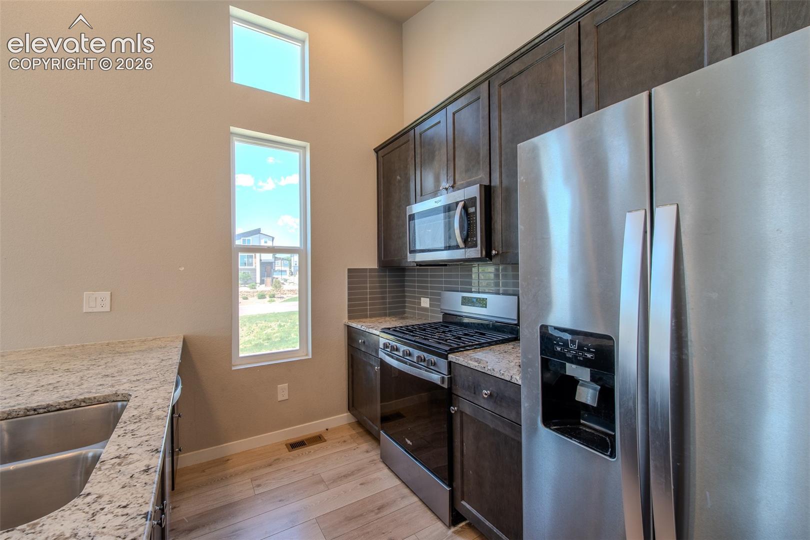 Double stainless steel sink, gas range oven, built-in microwave, and side by side refrigerator.