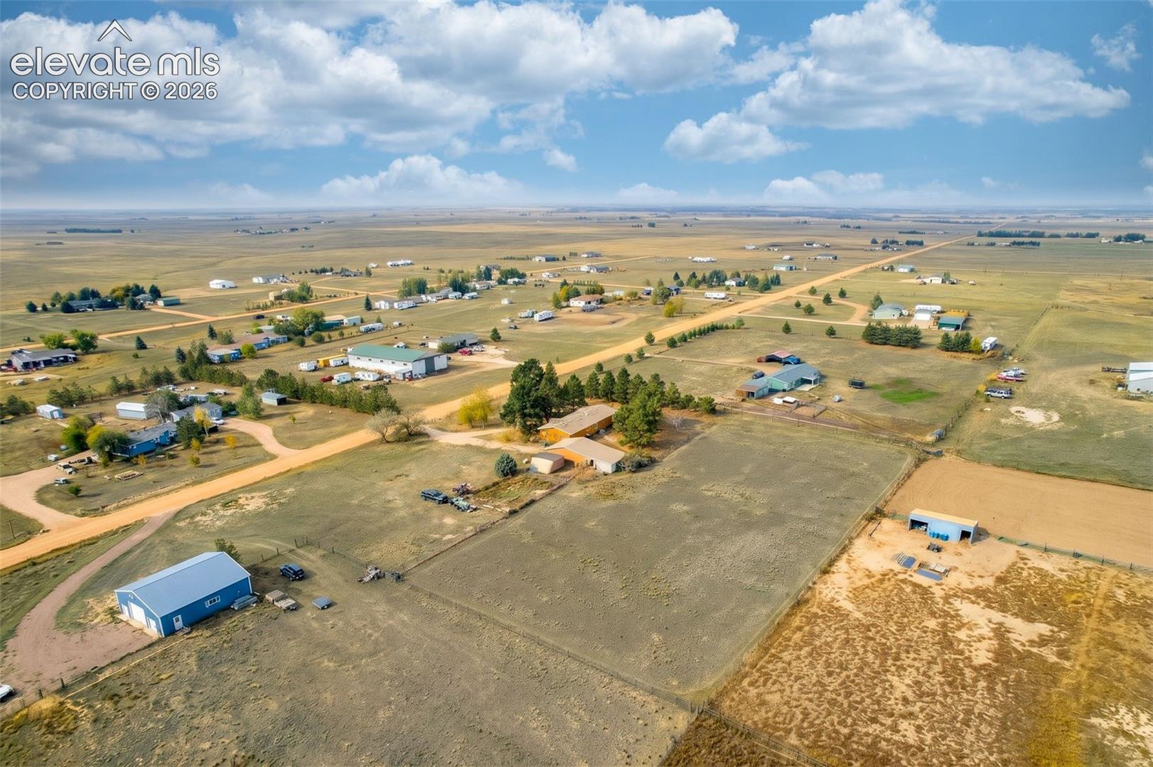 Expansive rural acreage featuring a detached metal-sided building, fenced perimeter, mature evergreen trees, and gravel road access