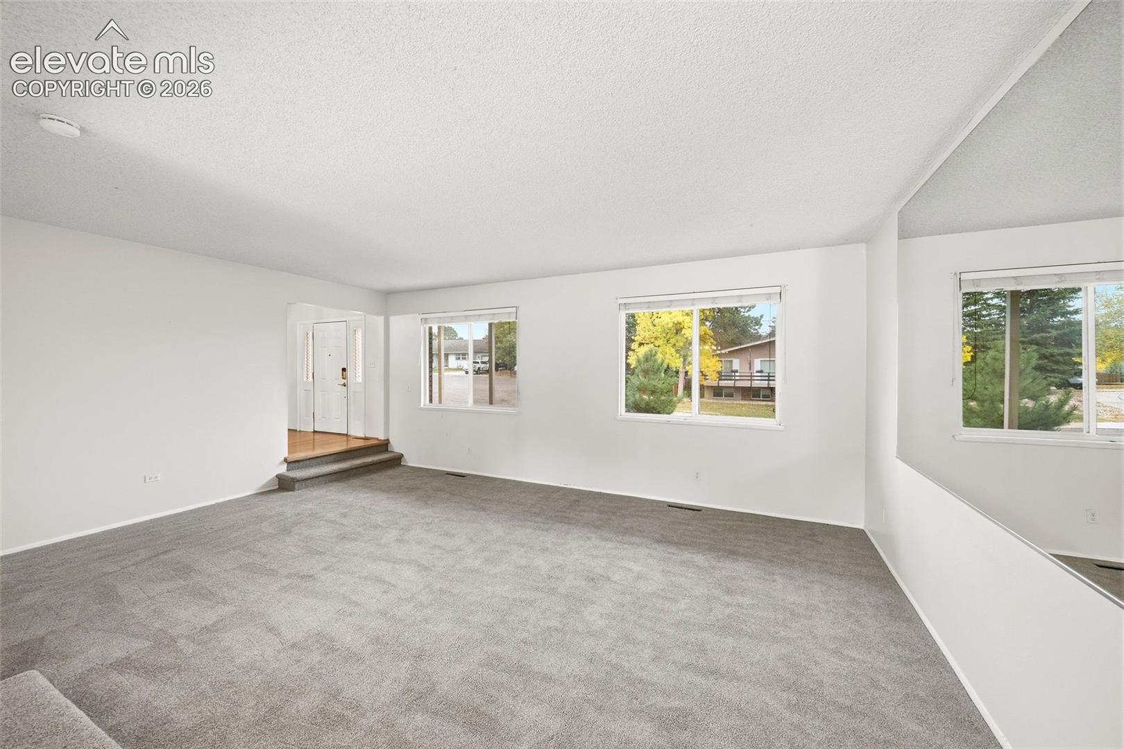 Neutral interior featuring wall-to-wall carpeting, expansive windows with natural light exposure, and a full-length wall mirror