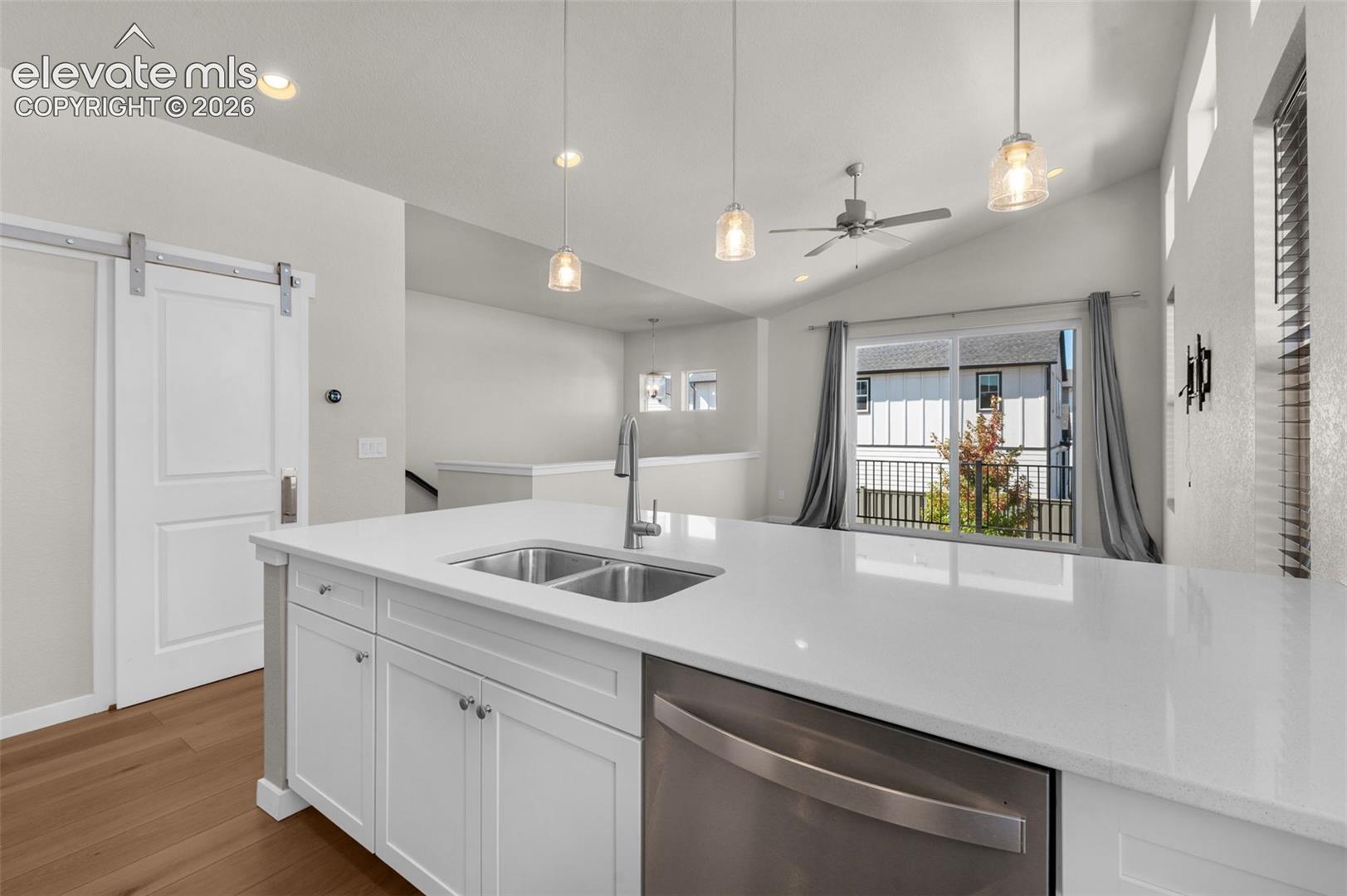 Kitchen featuring an expansive center island with solid-surface countertops, dual-basin stainless steel sink, wood-finish flooring, shaker-style cabinetry, and recessed pendant lighting