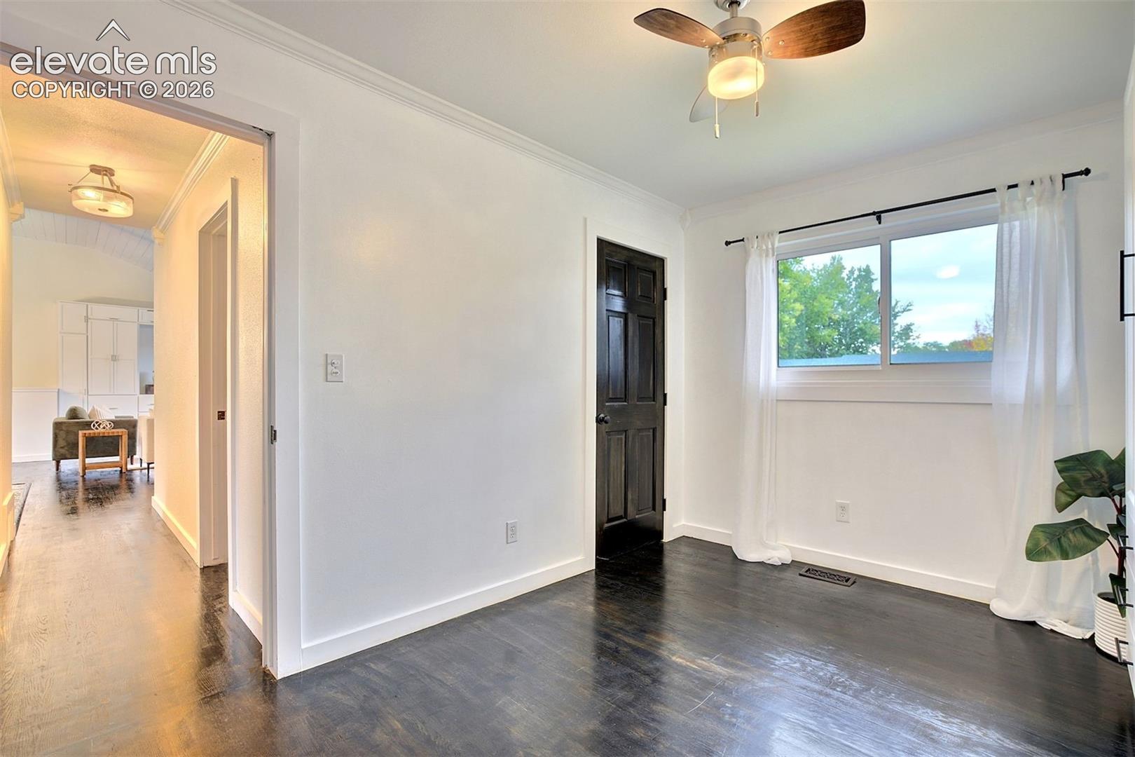 Dark wood-finish flooring, six-panel interior door with black finish, ceiling fan with light fixture, and horizontal slider window