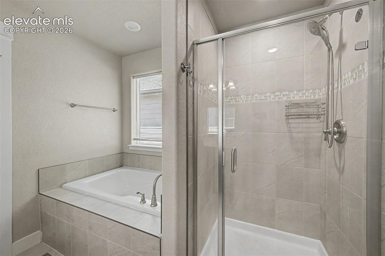 Bathroom featuring a glass-enclosed shower with tile surround, a built-in tub, and brushed nickel fixtures