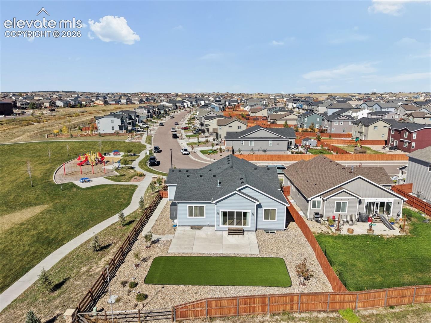 Aerial perspective of a single-story residence featuring a concrete patio, synthetic turf lawn, stone-surfaced landscaping, and a fenced backyard