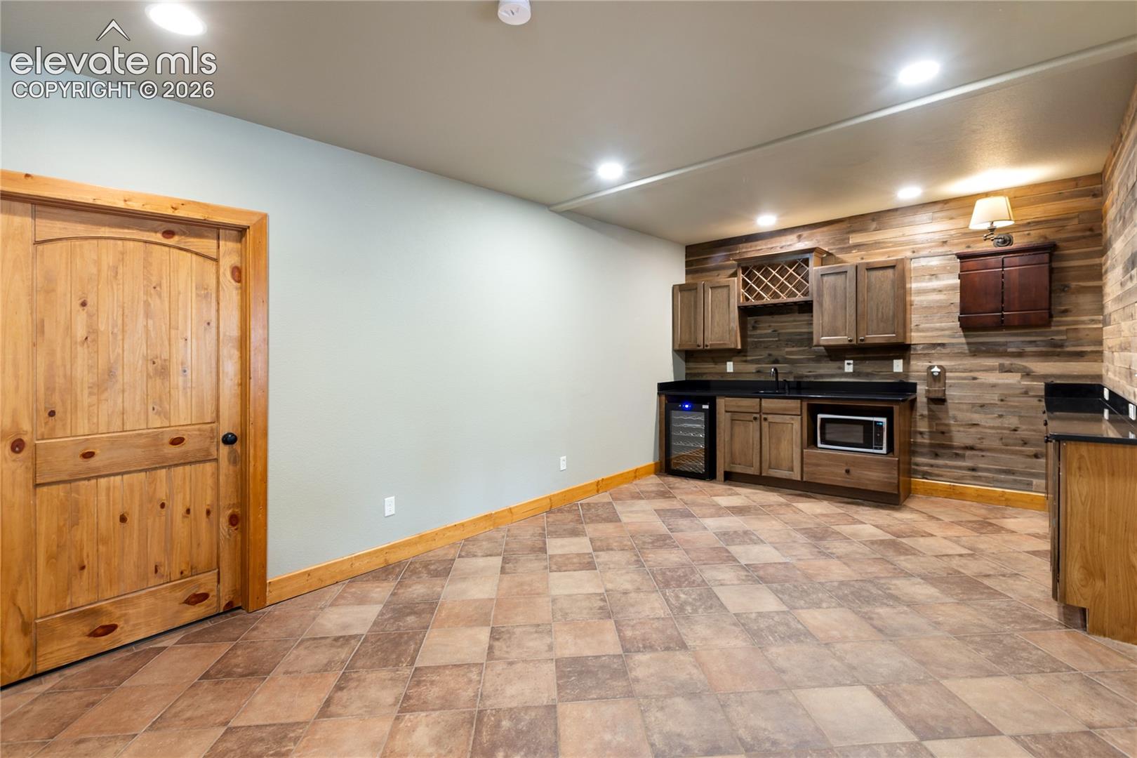 Built-in cabinetry with integrated wine storage, recessed lighting, wood-plank wall accents, and a solid wood door featuring a knotty finish