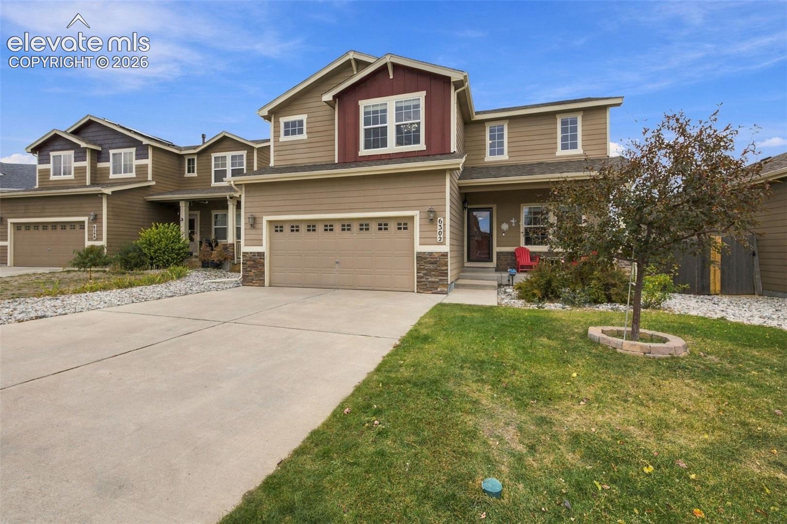 Two-story exterior featuring horizontal siding, stone veneer accents, an attached multi-car garage, and a front concrete driveway