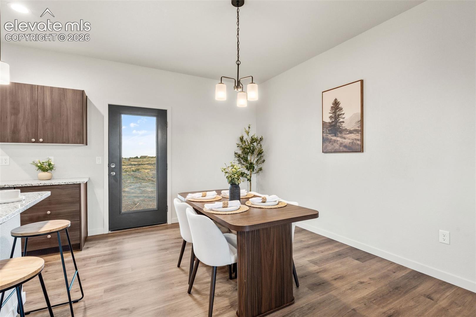 Wood-finish flooring, dark-toned cabinetry, stone-finish countertops, three-light hanging fixture, and exterior glass-paneled door