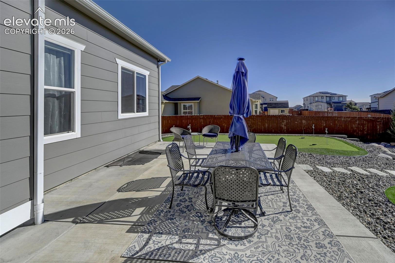 Expansive concrete patio with a decorative area rug, leading to a putting green and a landscaped area with stepping stones and dark gravel