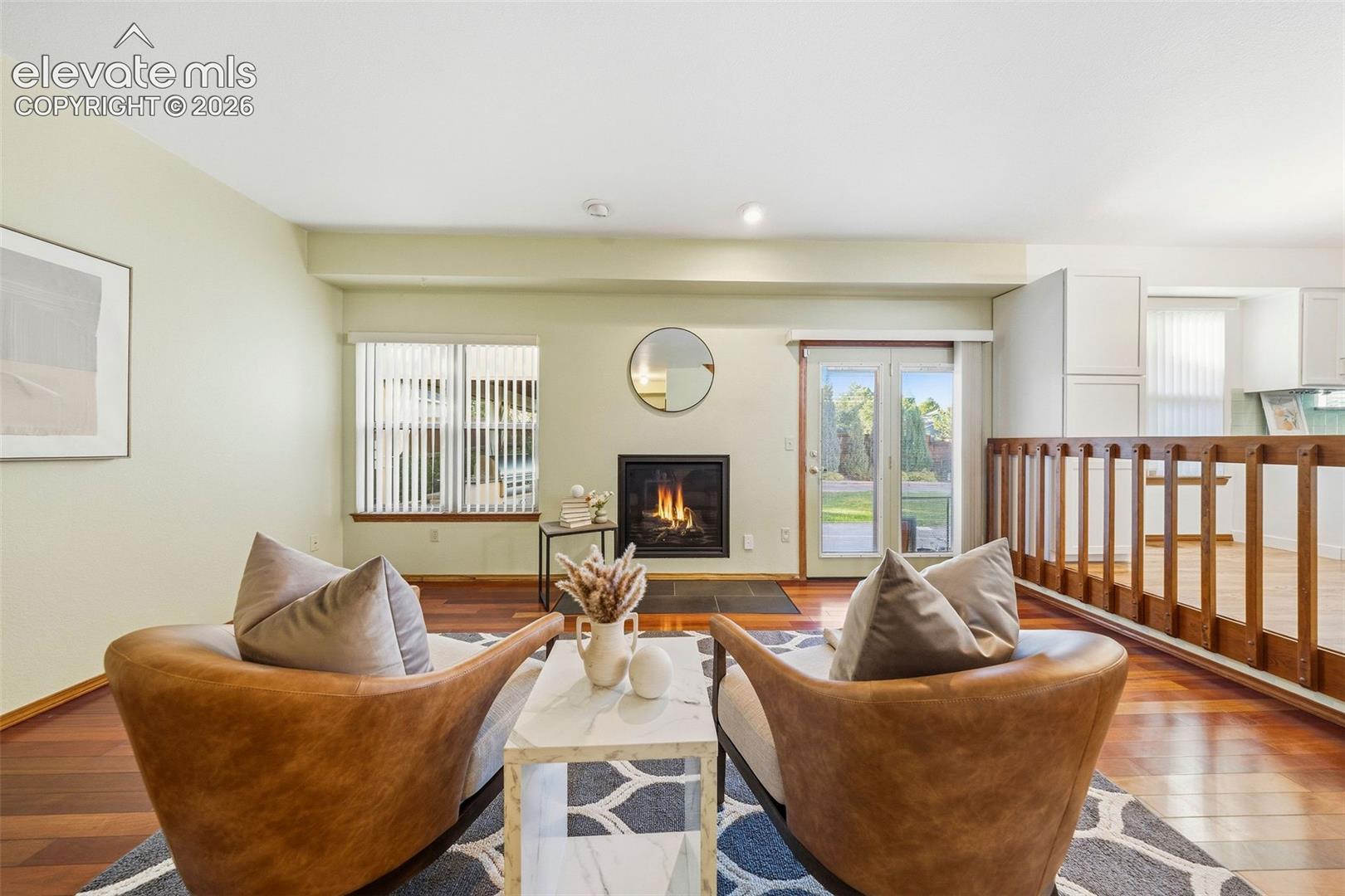 Living area featuring wood-finish flooring, a built-in fireplace with a stone-surround hearth, dual glass-paneled doors, and a wood railing