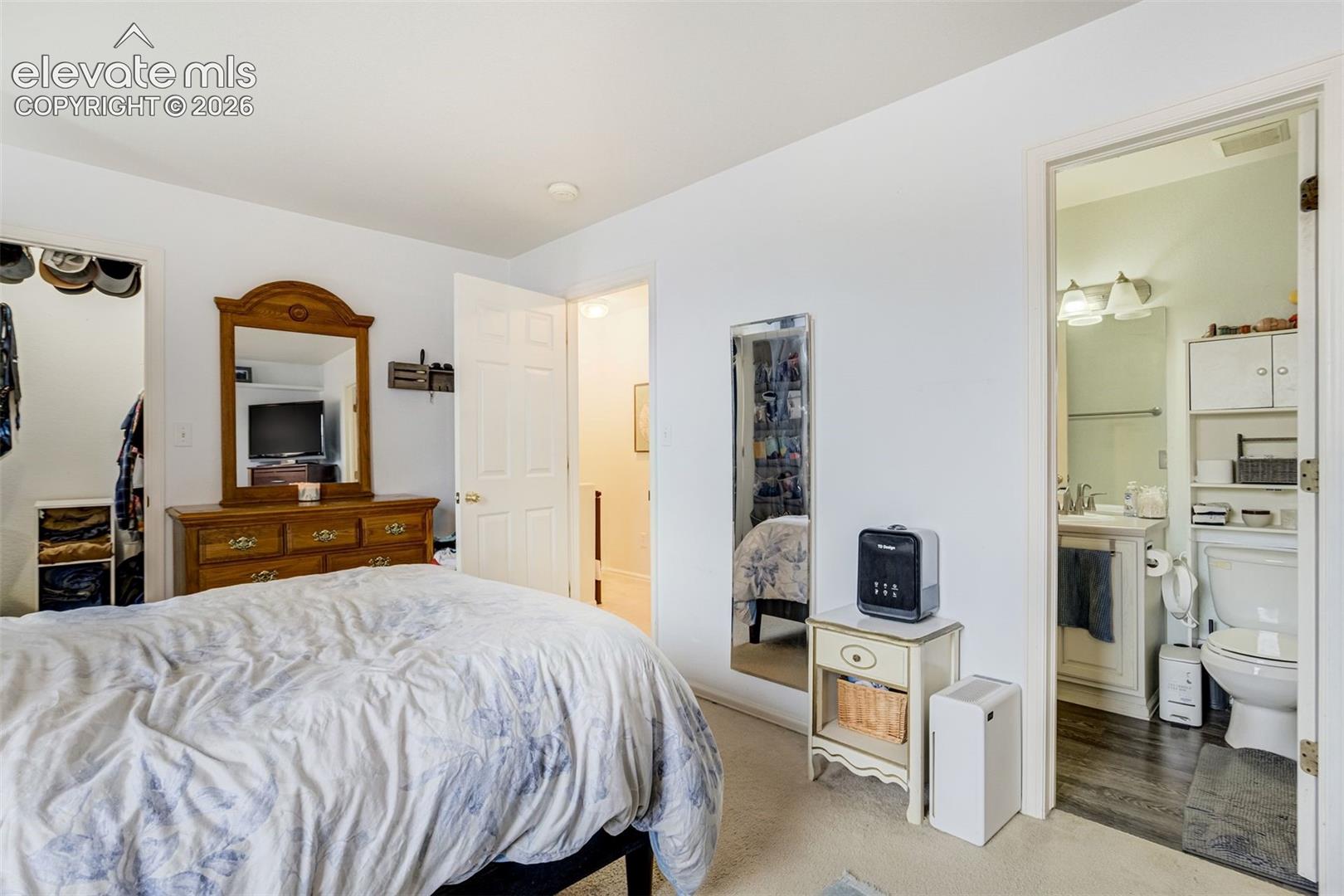Carpeted flooring, white walls, open doorway, built-in closet with shelving, and an adjoining bathroom with wood-finish flooring