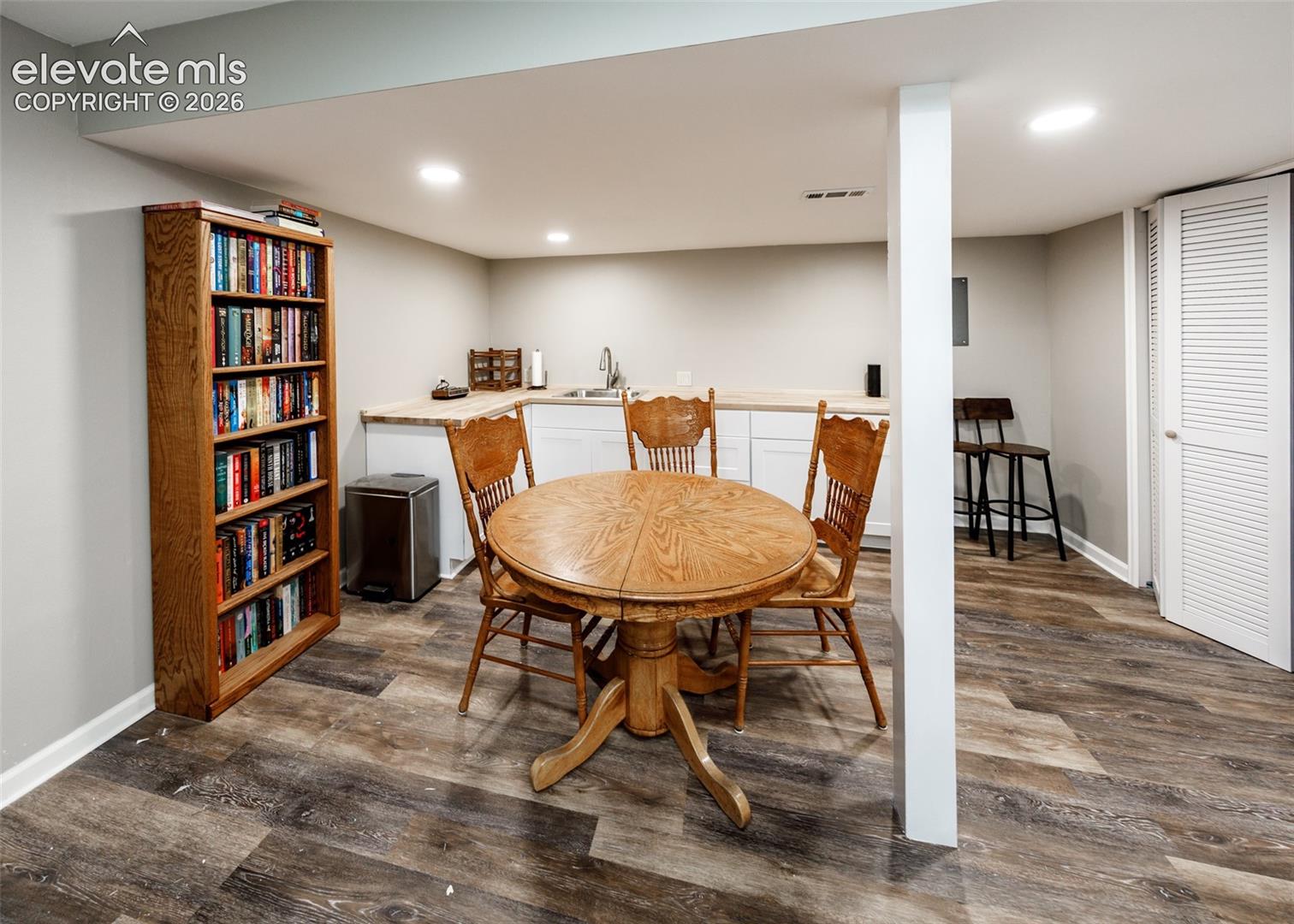 Recessed lighting illuminates the space, featuring wood-finish flooring, white cabinetry, and a stainless steel sink