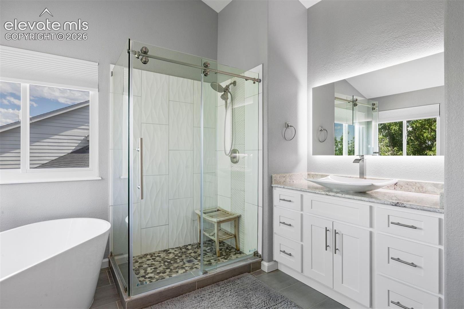 Vanity with a vessel sink, stone countertop, and an illuminated mirror