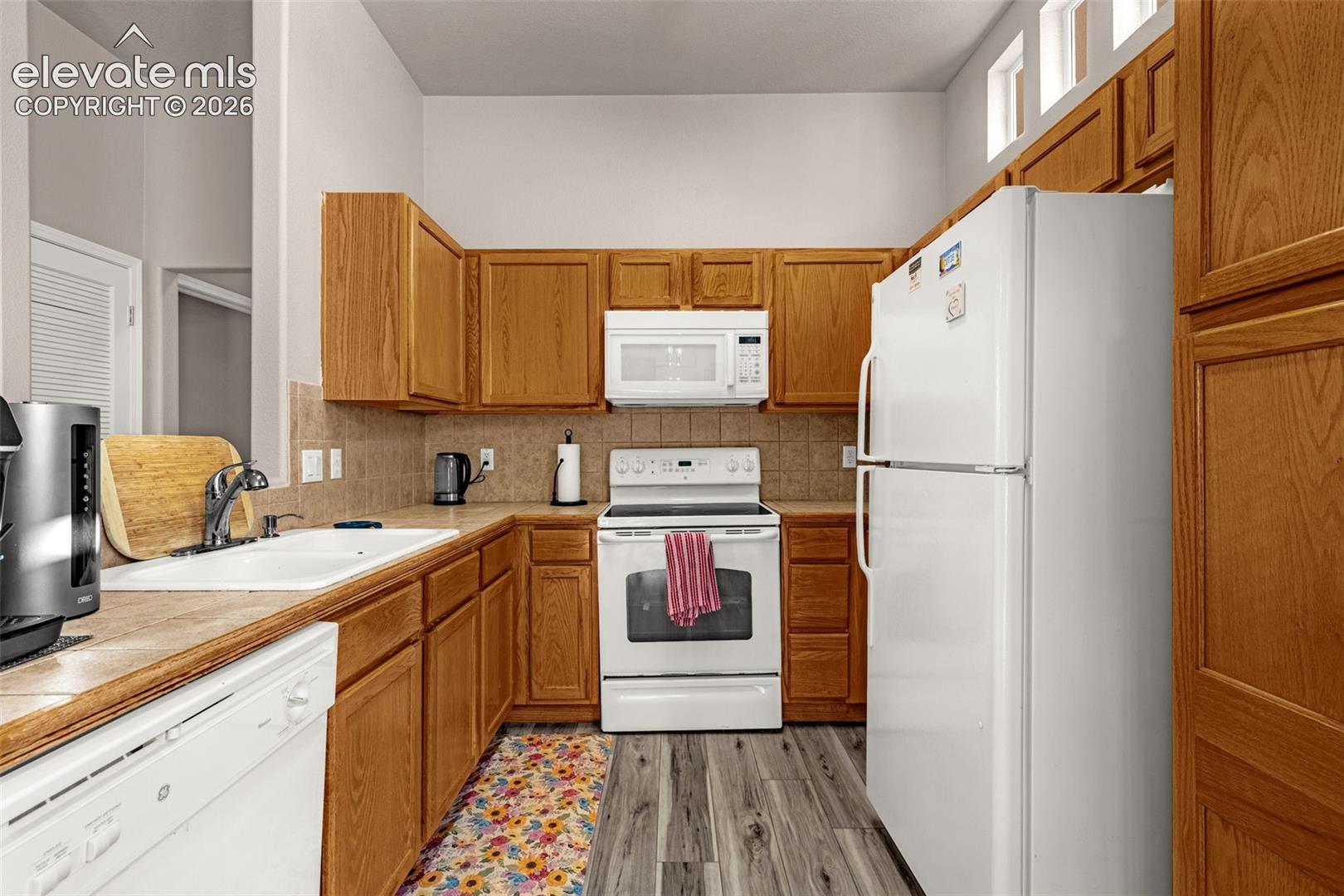 Kitchen featuring wood cabinetry, white appliances, tiled backsplash, dual-basin sink, and wood-finish flooring