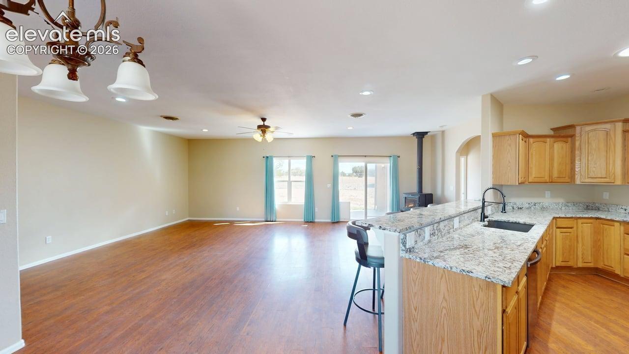 Open concept living area featuring wood-finish flooring, recessed lighting, and a kitchen with granite countertops, wood cabinetry, and a bar-height counter