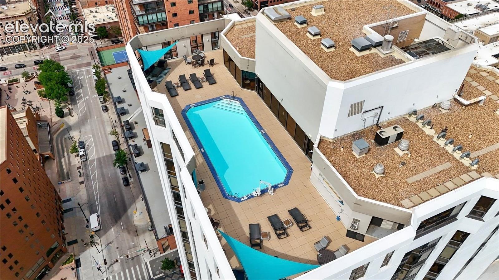 Rooftop swimming pool with a surrounding paved deck, complemented by shade sails and lounge areas