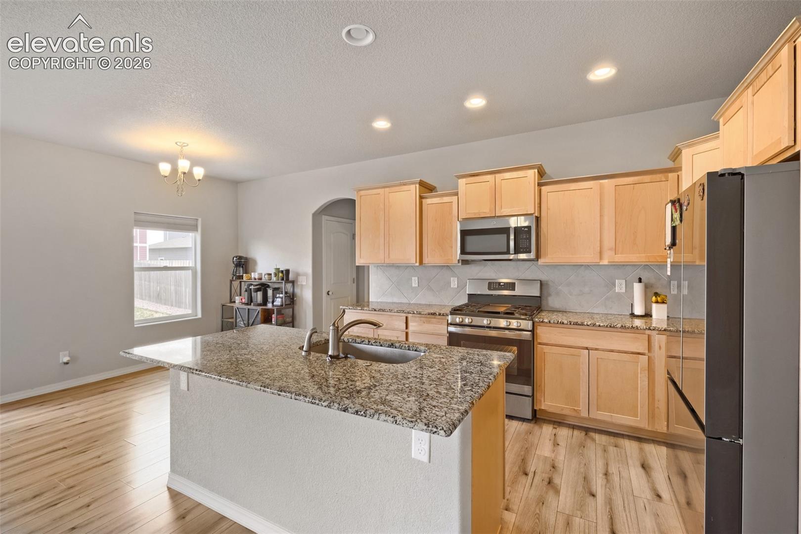 Kitchen featuring a central island with an undermount sink, granite countertops, wood-finish flooring, recessed lighting, and light wood cabinetry