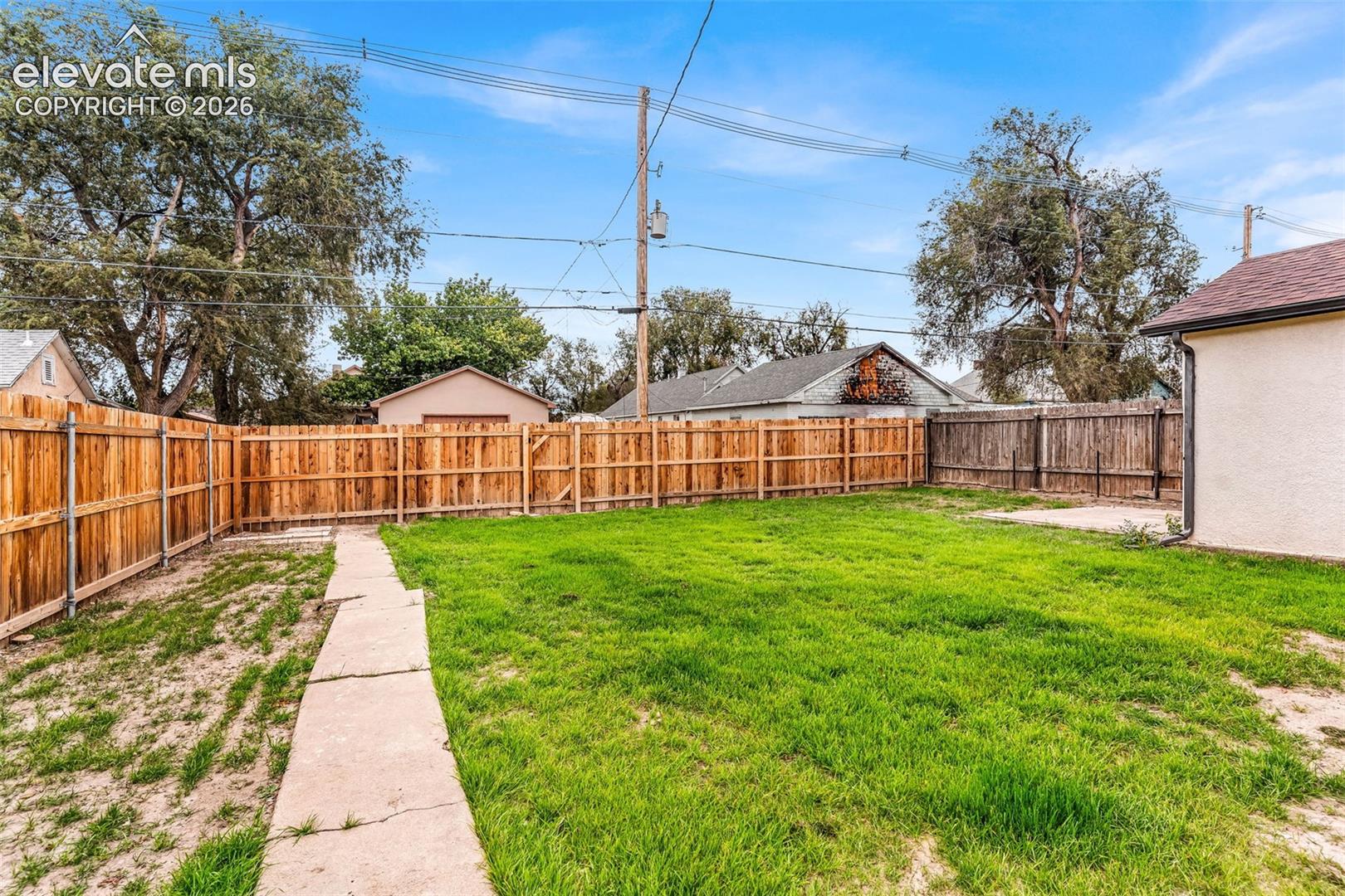 Fenced backyard featuring a grass lawn, concrete pathway, and perimeter wood fencing