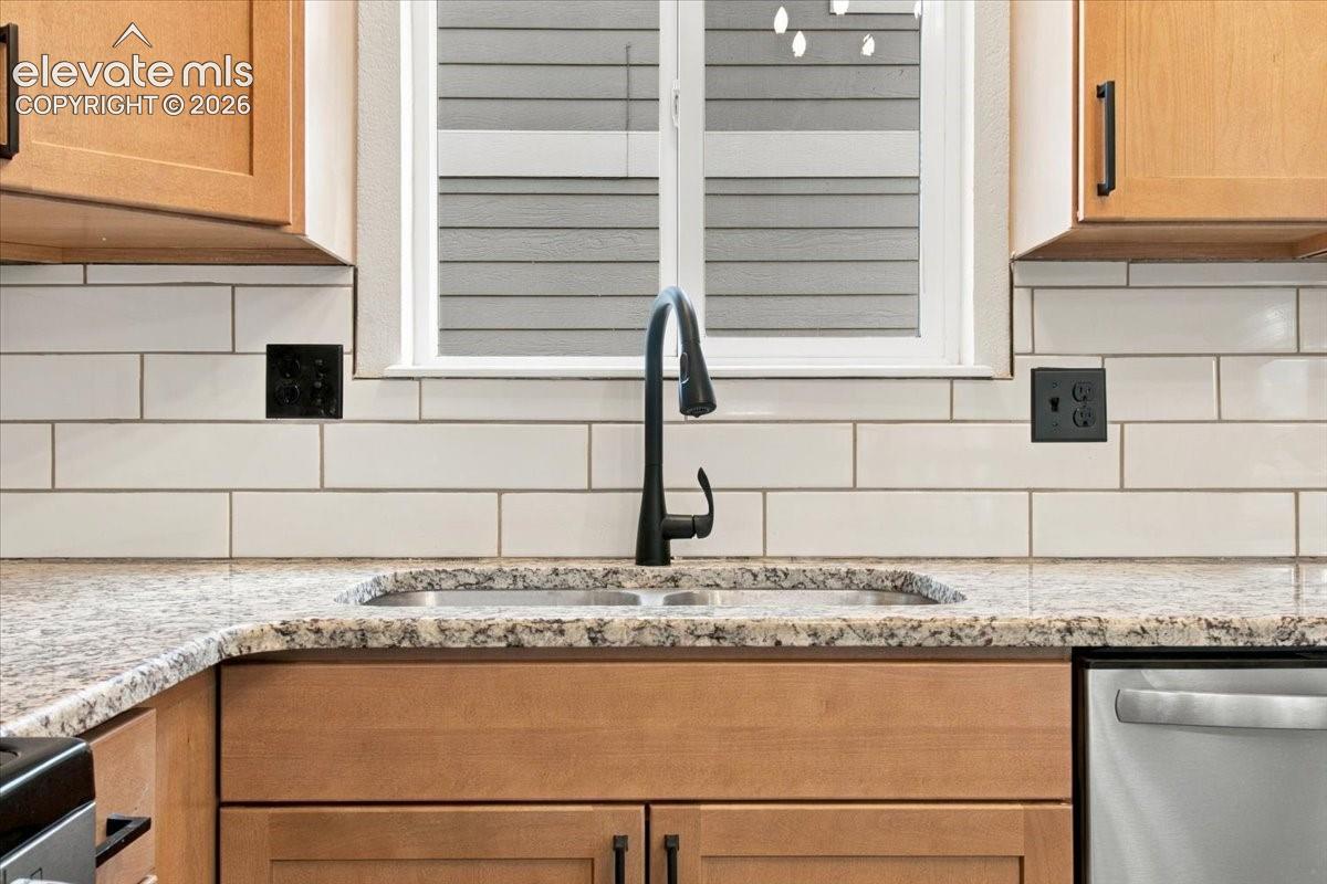 Kitchen featuring light-finish cabinetry with matte black hardware, stone-patterned countertops, a white subway tile backsplash, and a high-arch matte black faucet