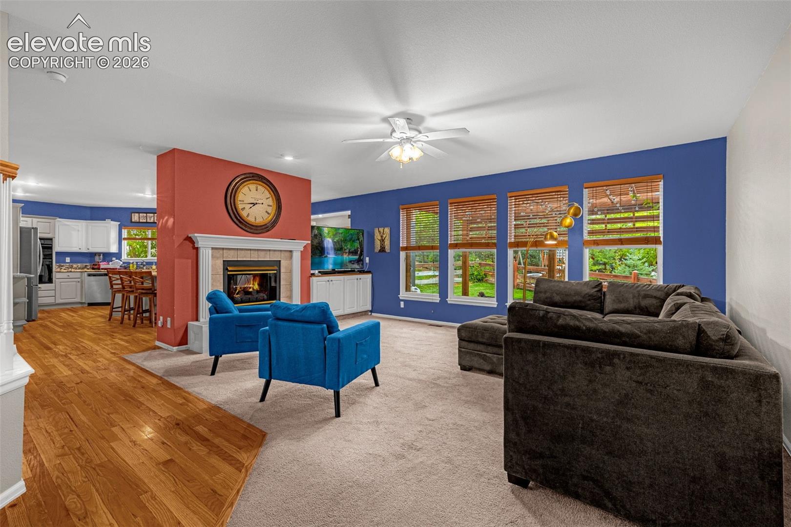 Wood-finish flooring, carpeted living area, fireplace with mantel, multiple windows, and a built-in entertainment cabinet