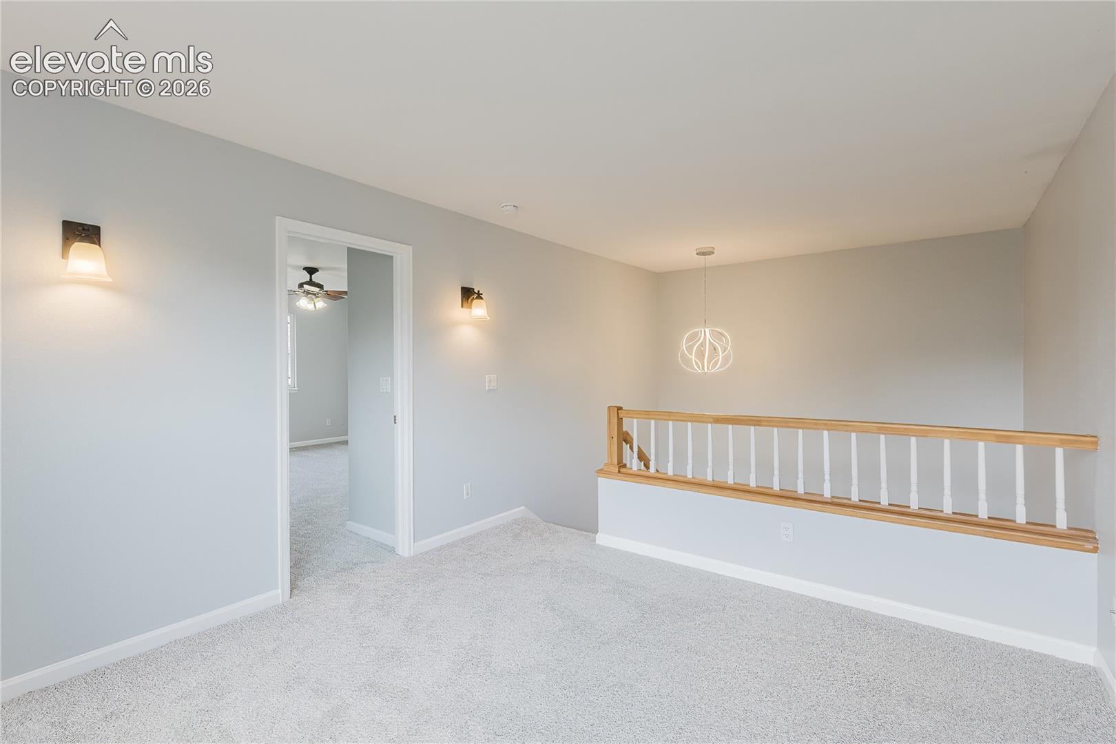 Neutral carpeting, wood handrail with white balusters, and contemporary pendant lighting